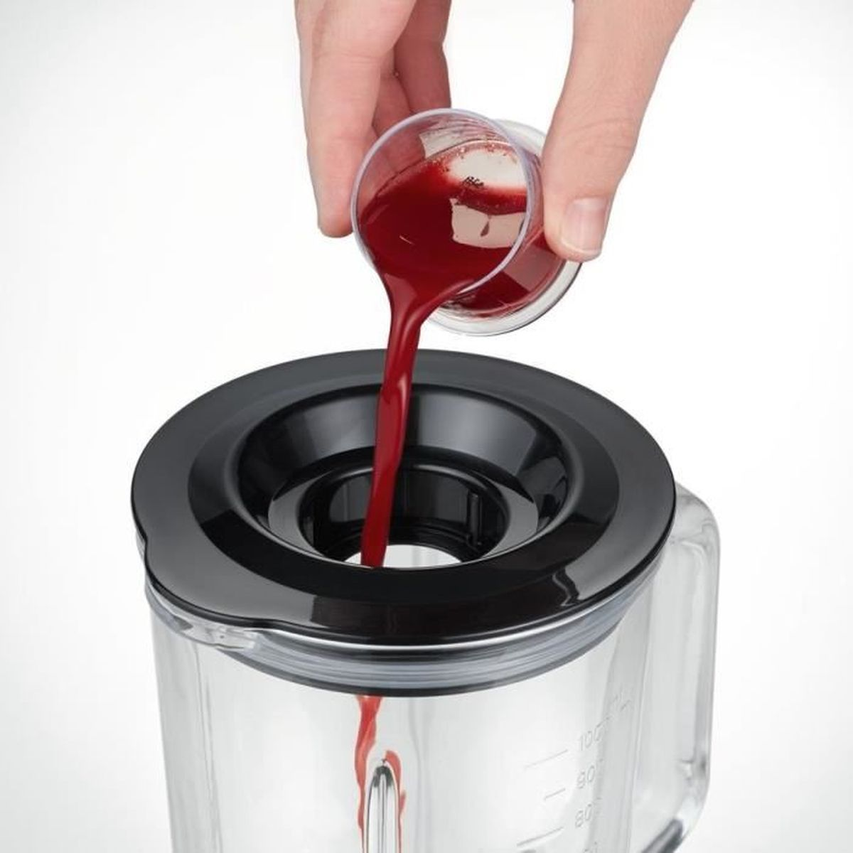 Eine Hand gießt rote Flüssigkeit aus einem Messbecher in einen Glas-Mixerbehälter.