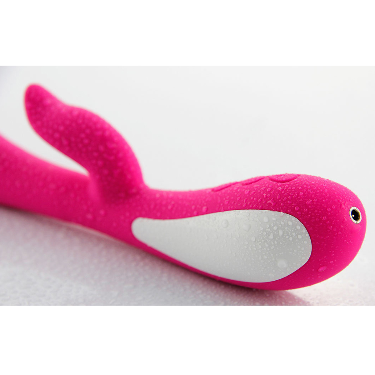 Pinker Vibrator mit weißen Akzenten. Es hat ein gebogenes Design und ist mit Wassertropfen bedeckt.