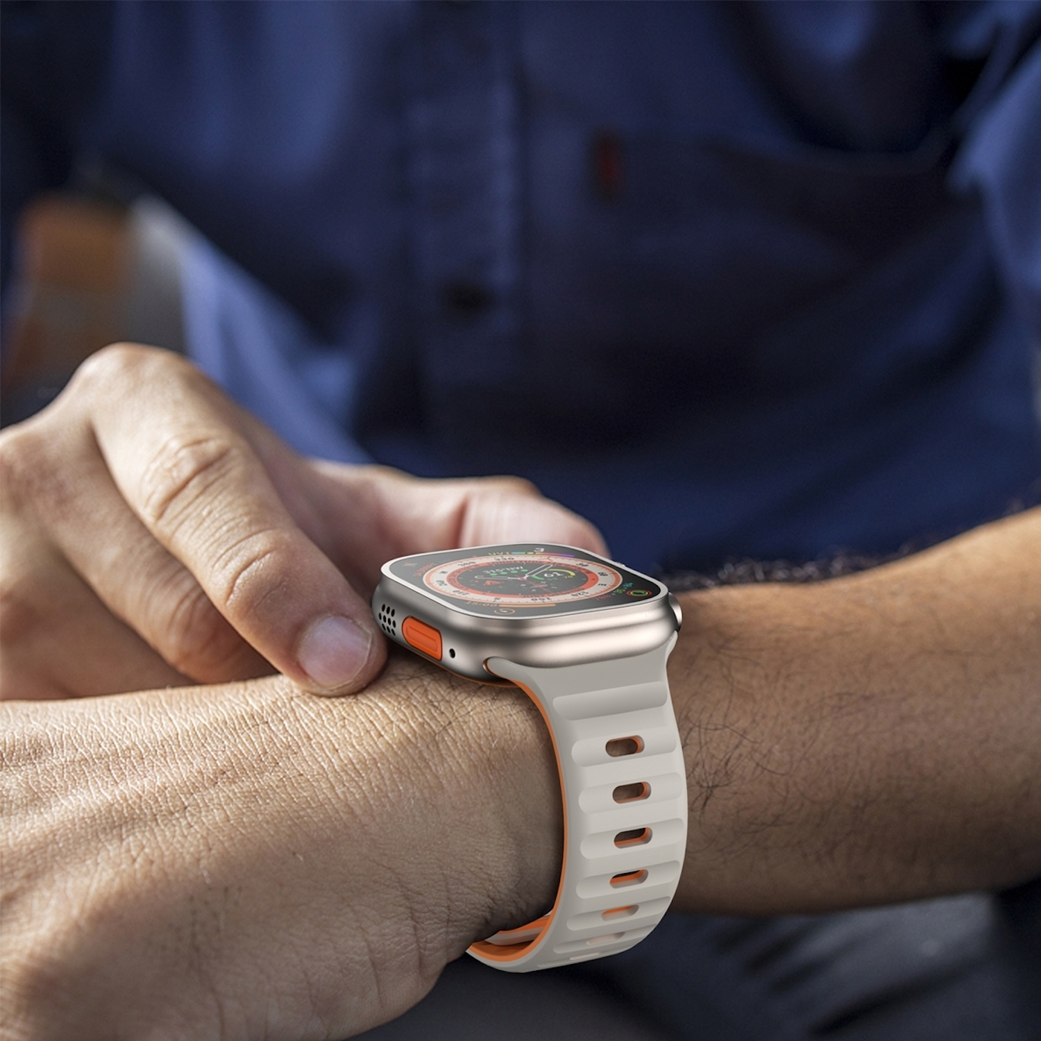 Das Handgelenk eines Mannes mit einer silbernen und orangefarbenen Smartwatch. Das Armband ist weiß.
