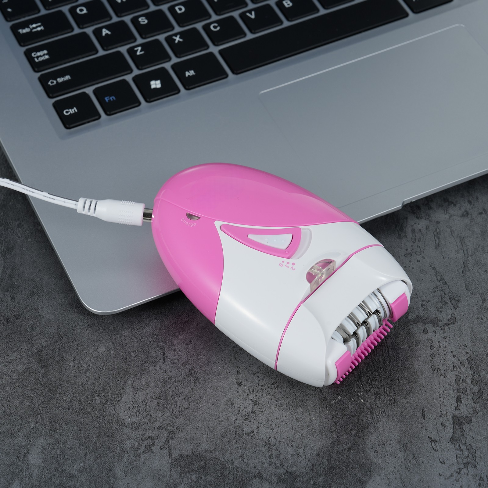 Rosa und weißer Epilierer, der an einem Laptop auf einer grauen Oberfläche angeschlossen ist.