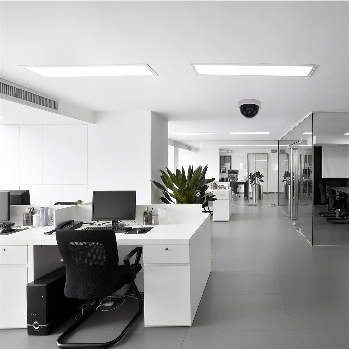 Modernes Bürointerieur mit weißen Wänden, Schreibtischen und einer Überwachungskamera an der Decke. Pflanze im Hintergrund.
