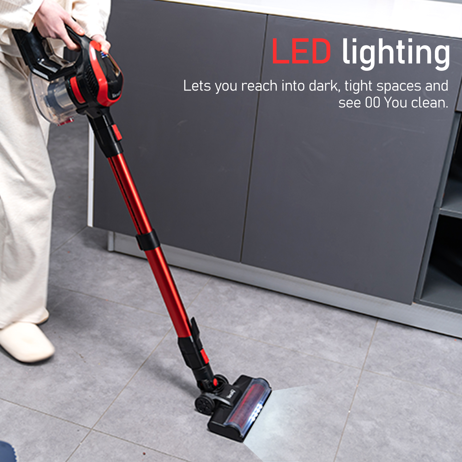 Czerwono-czarny odkurzacz czyszczący szarą podłogę. Świeci światło LED.