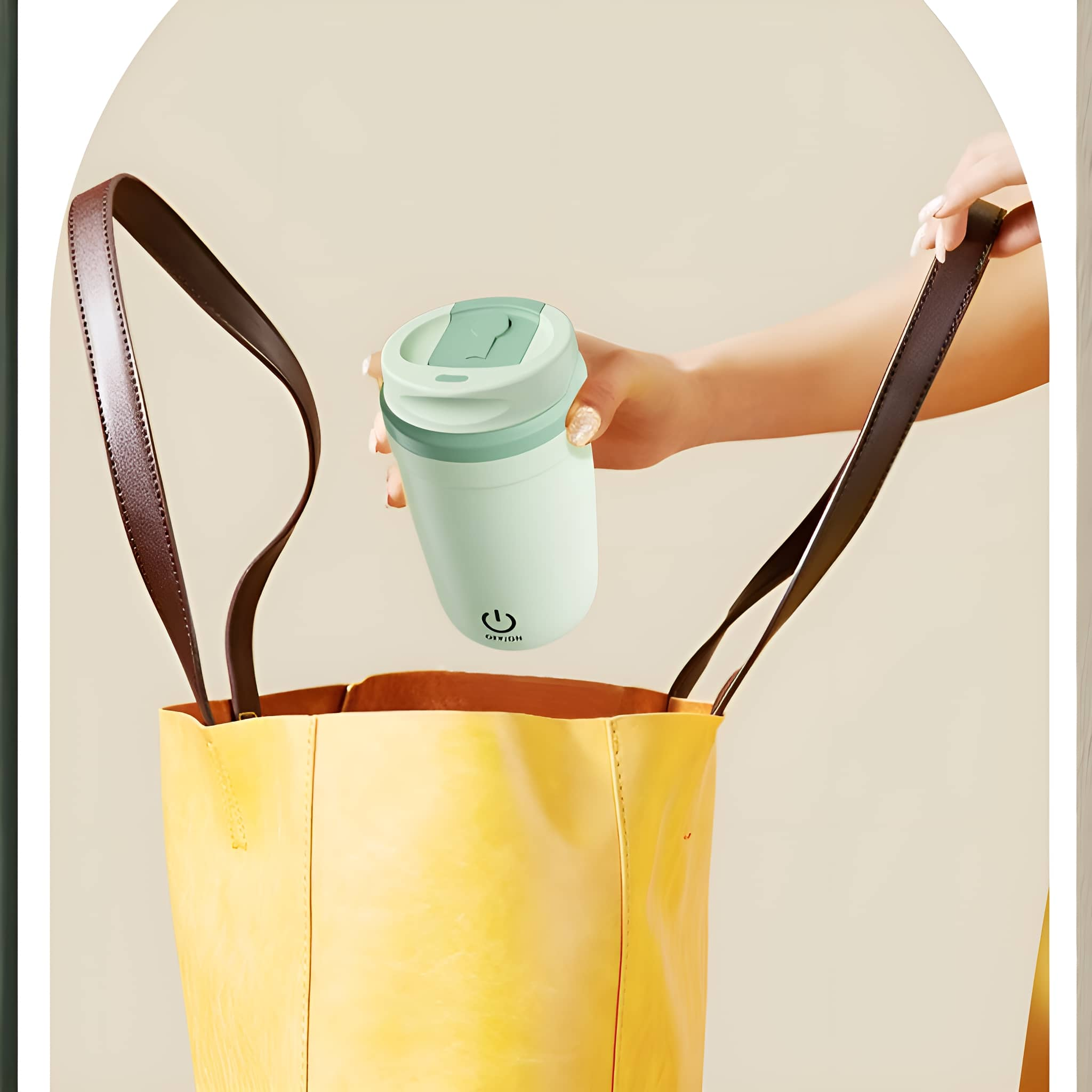 Eine Person hält einen mintgrünen Reisebecher und legt ihn in eine gelbe Handtasche. Braune Träger.