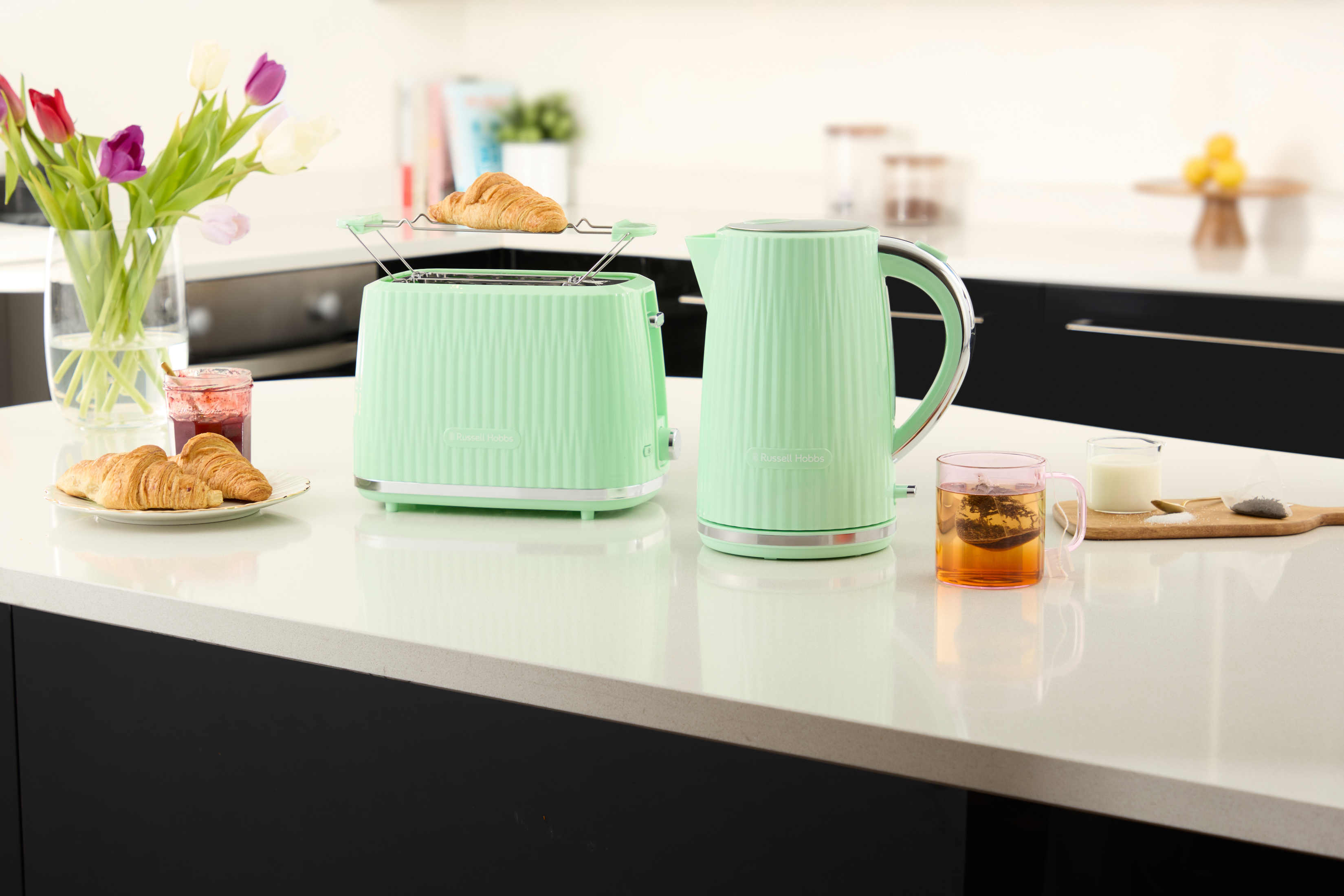 Bancone della cucina con tostapane, bollitore, croissant e tè. Tulipani in un vaso a sinistra.