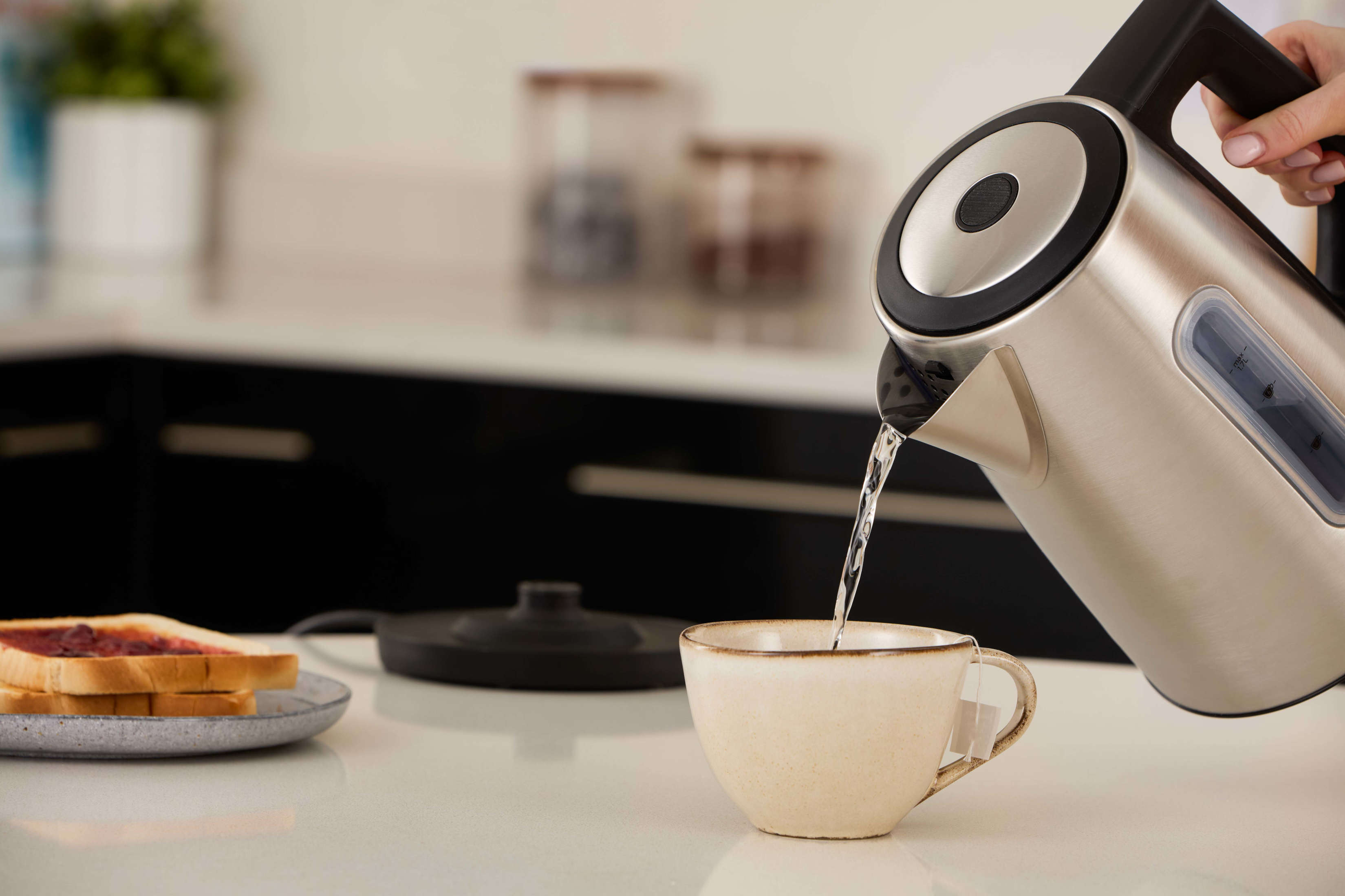 Edelstahl-Wasserkocher gießt Wasser in eine Tasse auf weißer Arbeitsplatte.