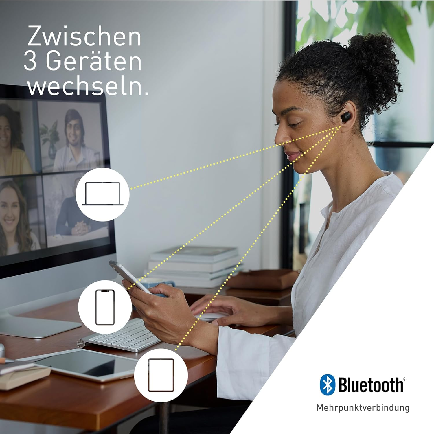Una donna indossa auricolari, guardando uno schermo che mostra una videoconferenza. Vengono mostrati più dispositivi.