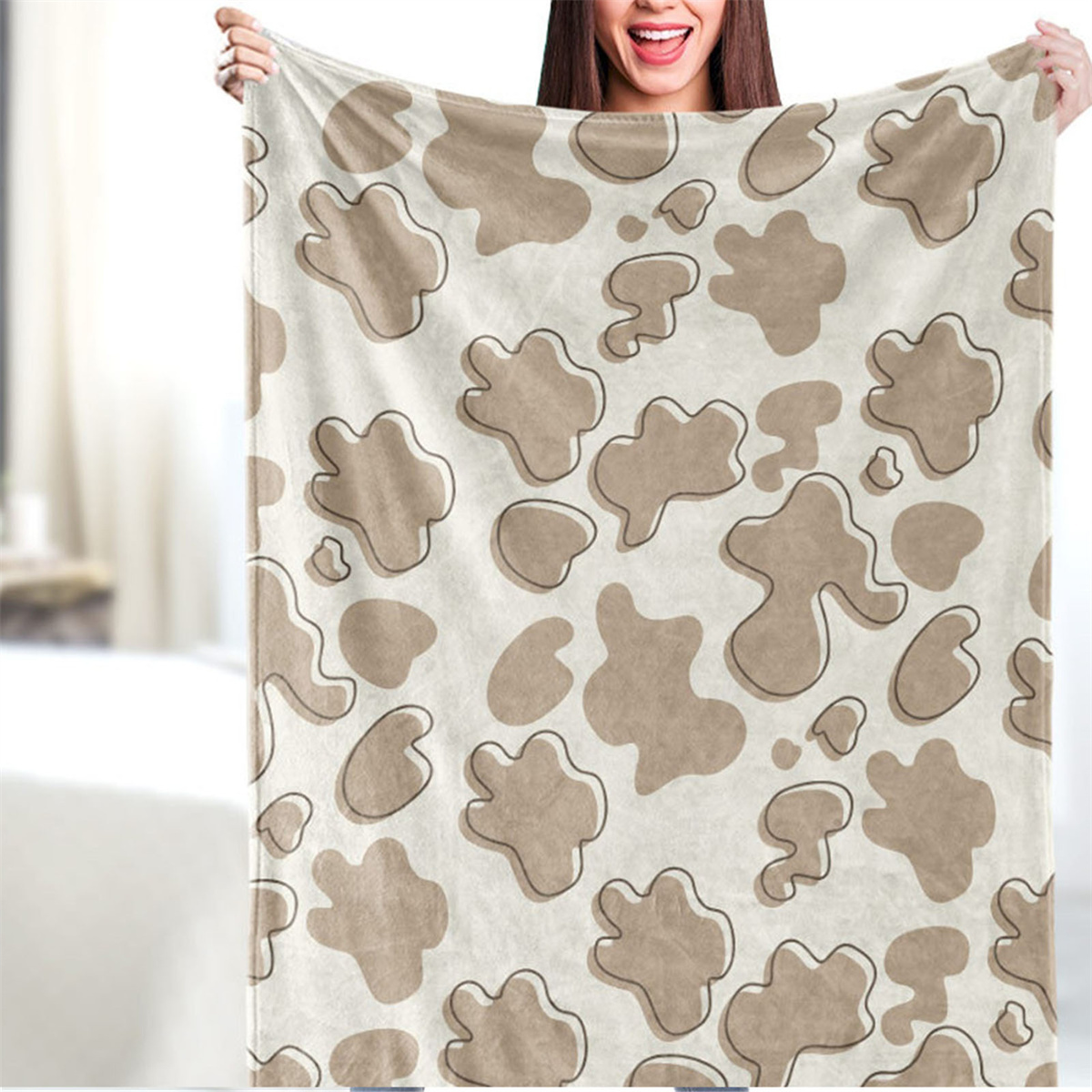 Eine Frau hält eine beige Decke mit braunen Flecken vor weißem Hintergrund.