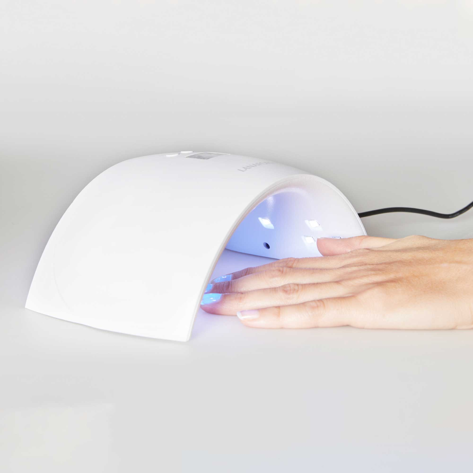 Weiße Nagelhärtungslampe mit einer Hand darin. Die Nägel sind hellblau lackiert.