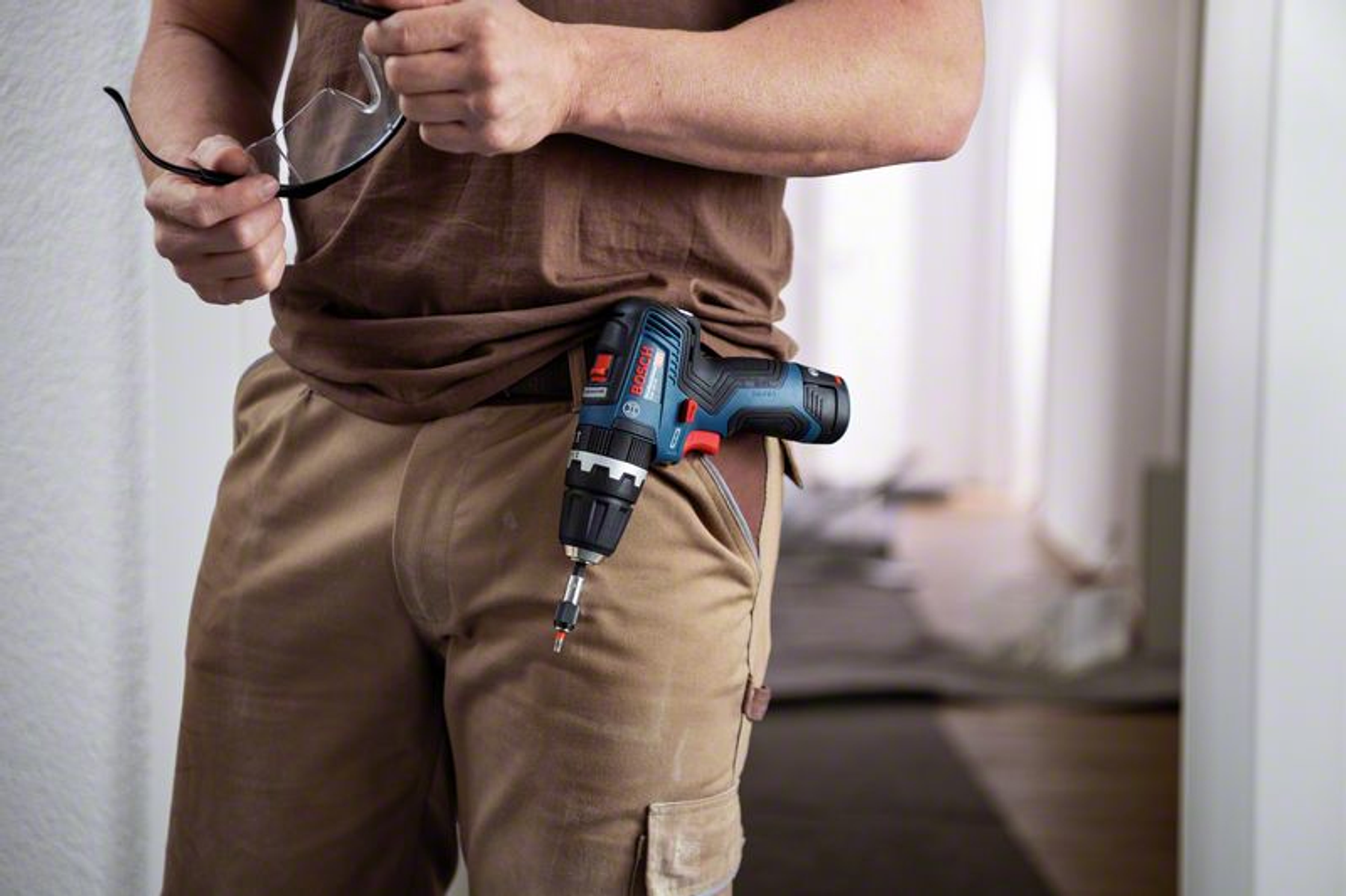 Mężczyzna trzymający okulary i wiertarkę w kieszeni.