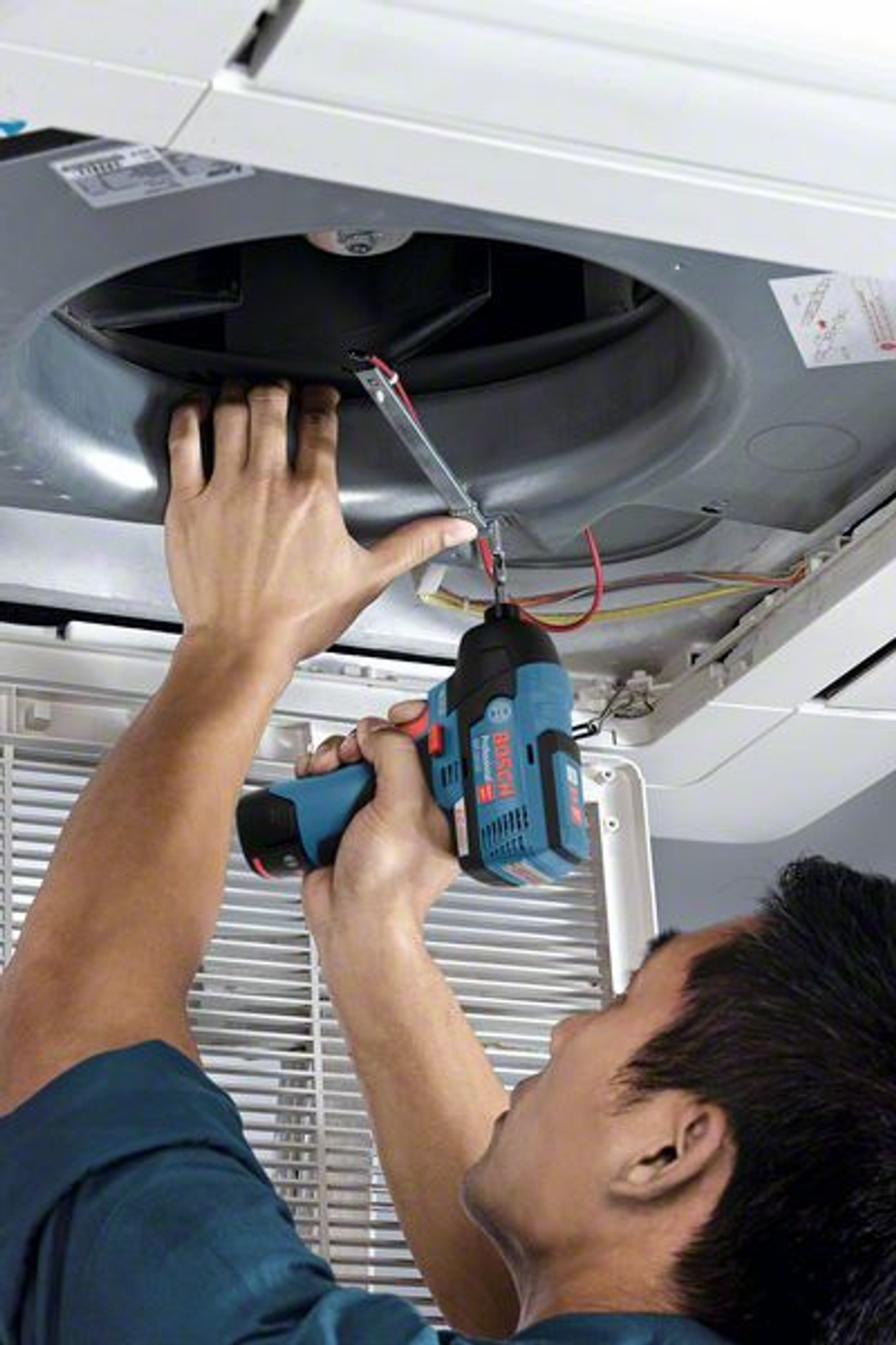 Mężczyzna pracujący przy jednostce klimatyzacji z elektronarzędziem. Widok z bliska.