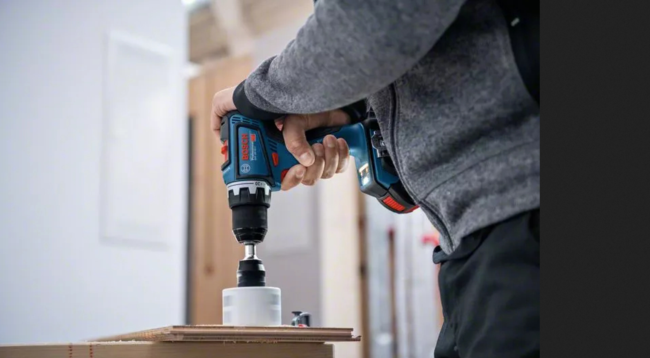 Osoba używająca niebiesko-czarnej wiertarki Bosch do wiercenia otworu w drewnie.