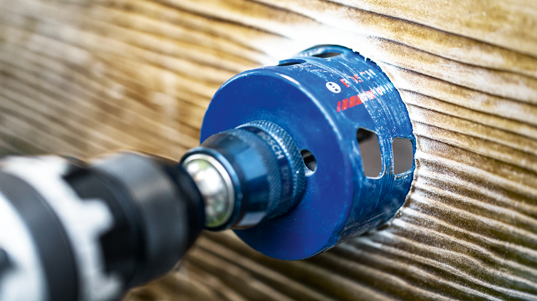 Niebieska piła otwornica wiercąca w drewnianej powierzchni. Widoczna wiertarka.