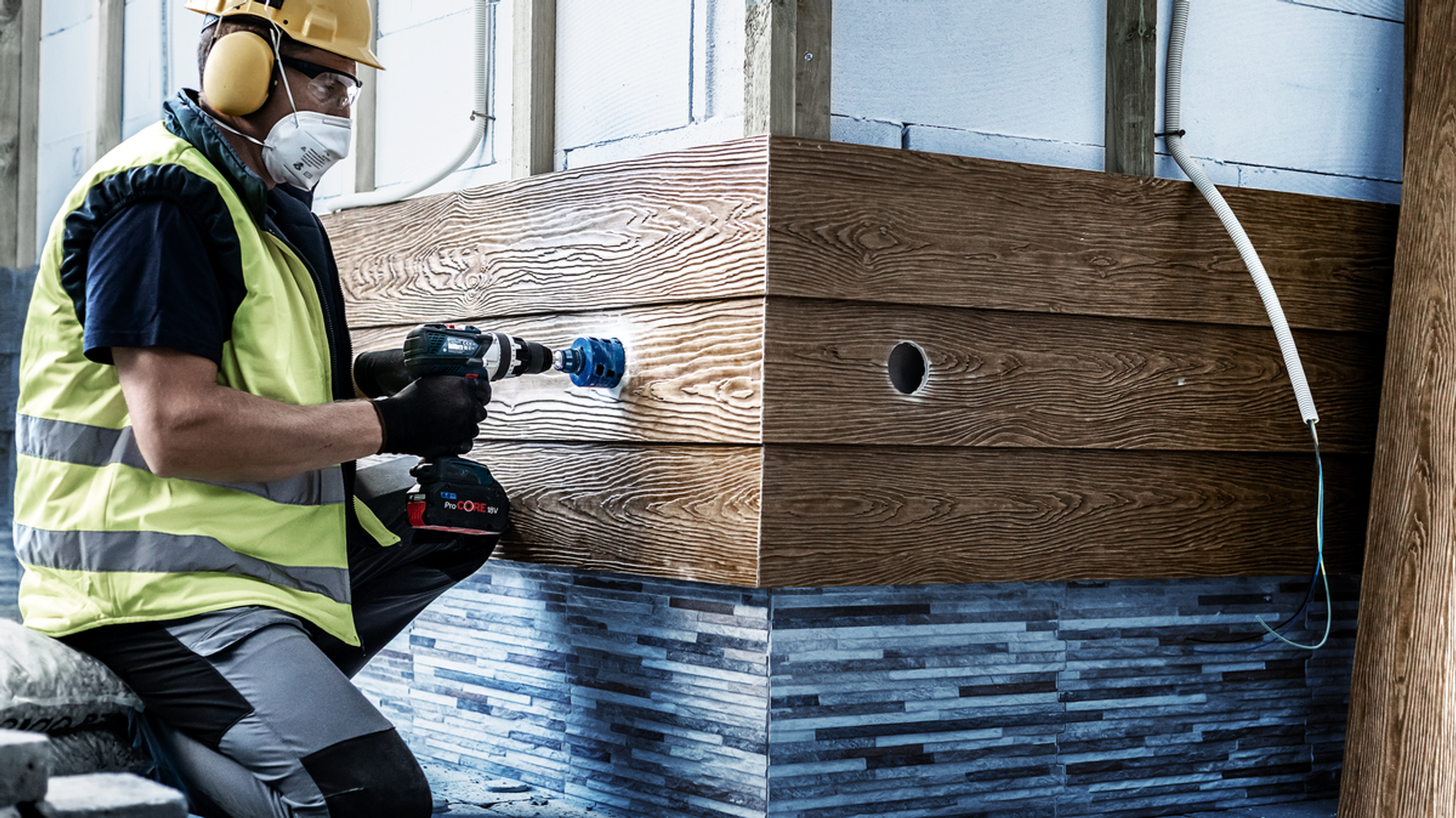 Pracownik wiercący w drewnie. Pracownik nosi sprzęt ochronny i wierci w drewnianym panelu.