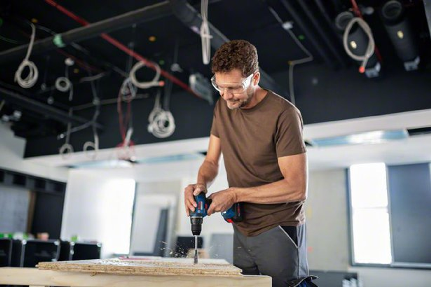 Mężczyzna używa wiertarki, aby zrobić otwór w drewnianej desce.