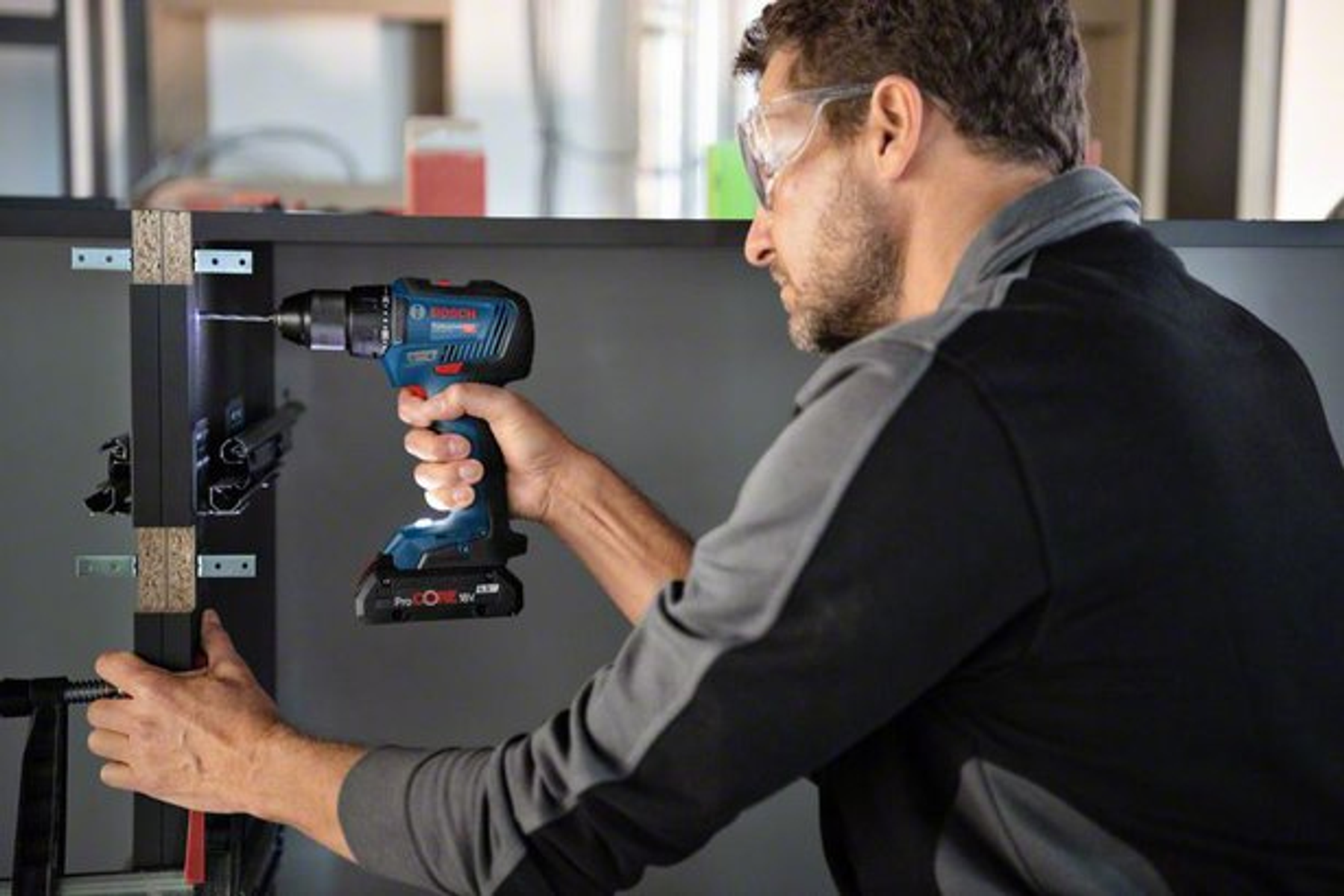 Mężczyzna używający niebiesko-czarnej wiertarki na czarnej szafce.