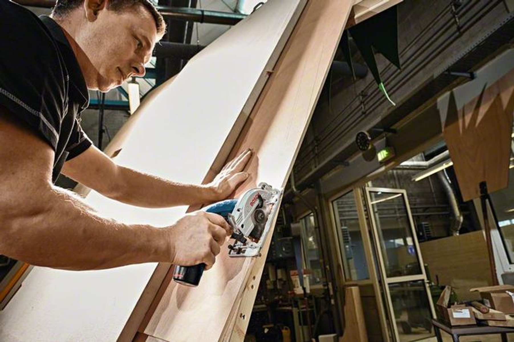 Mężczyzna używa piły tarczowej do cięcia drewna. Piła jest niebiesko-czarna, a drewno jasnobrązowe.