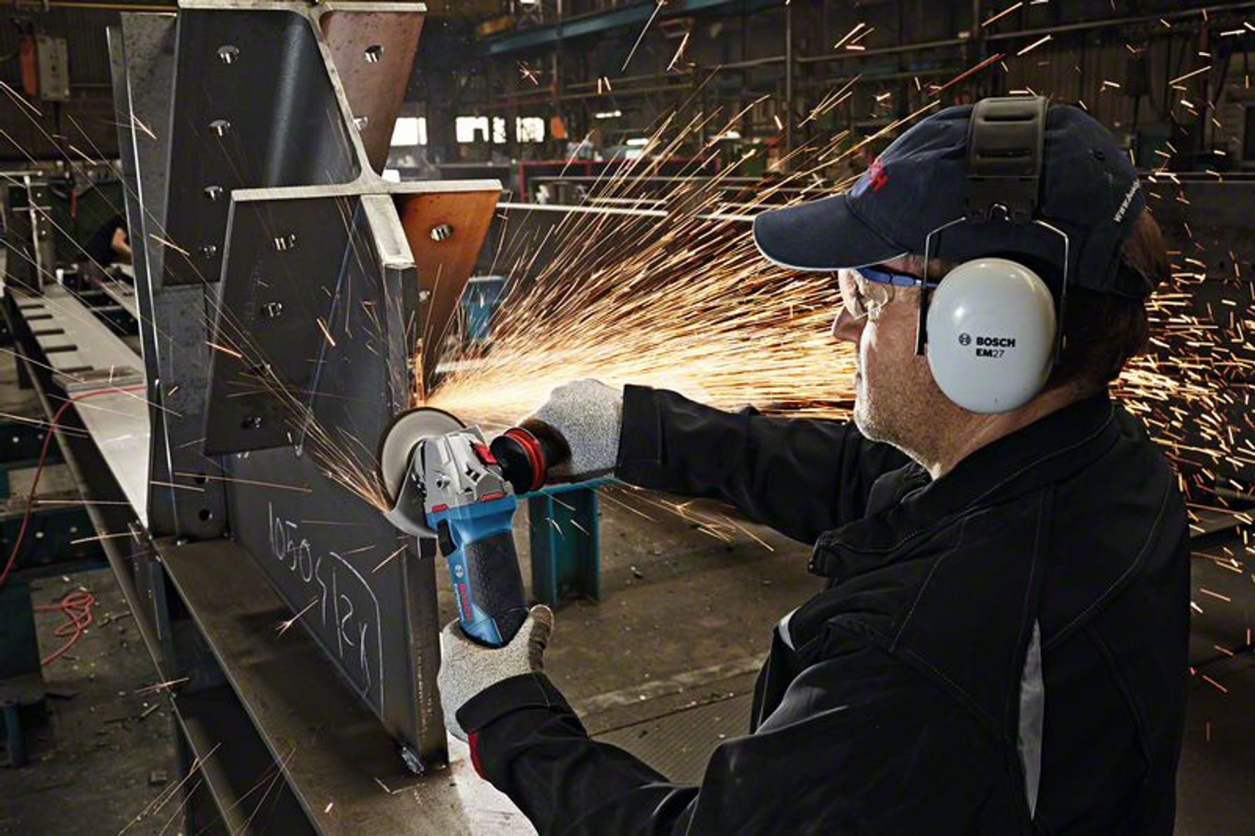 Ein Mann schleift Metall mit einer Schleifmaschine, Funken fliegen. Er trägt Schutz.