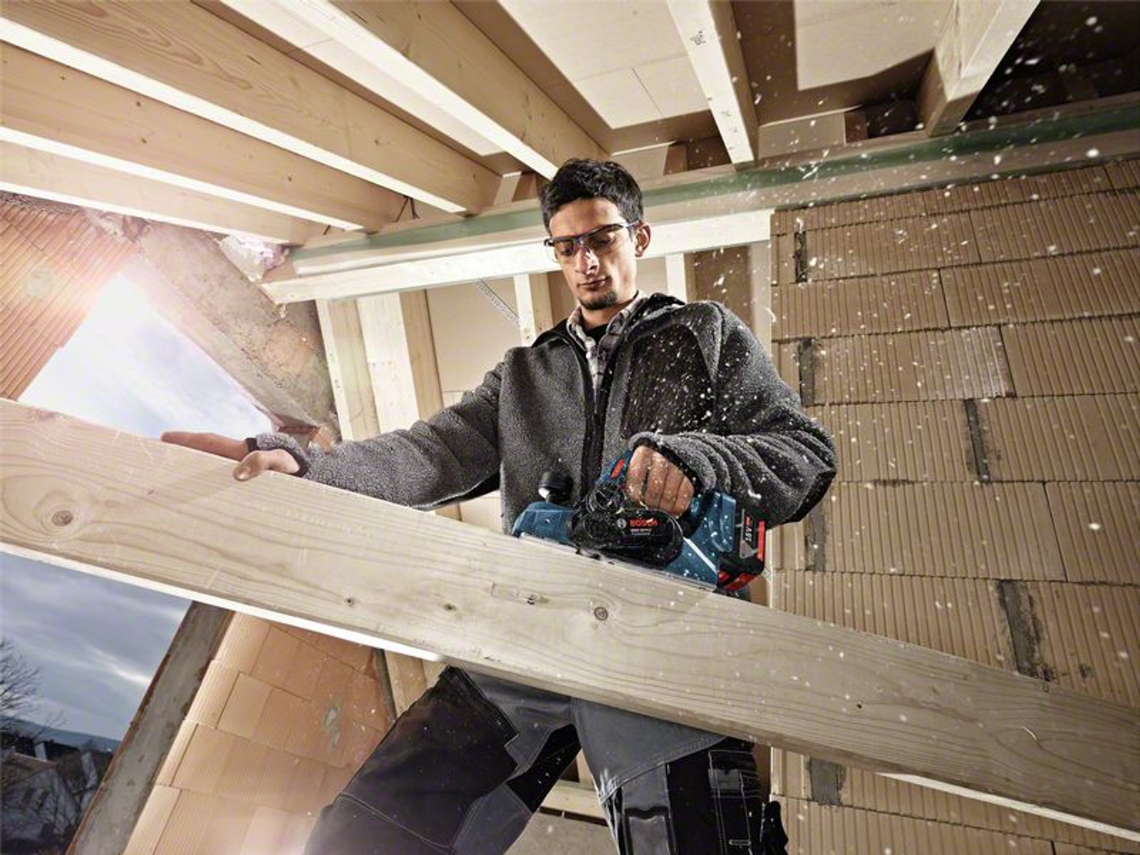 Ein Mann, der einen Elektrohobel an einem Holzbalken verwendet, mit Sägemehl in der Luft.