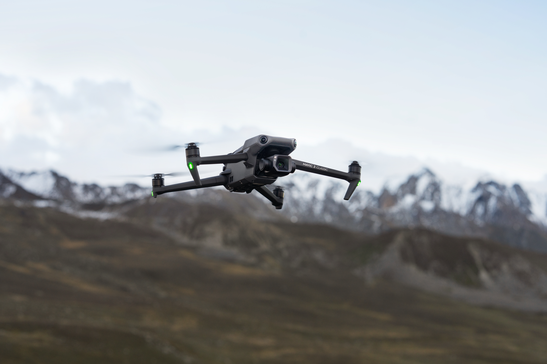 Schwarze Drohne im Flug. Berge im Hintergrund, bewölkter Himmel.