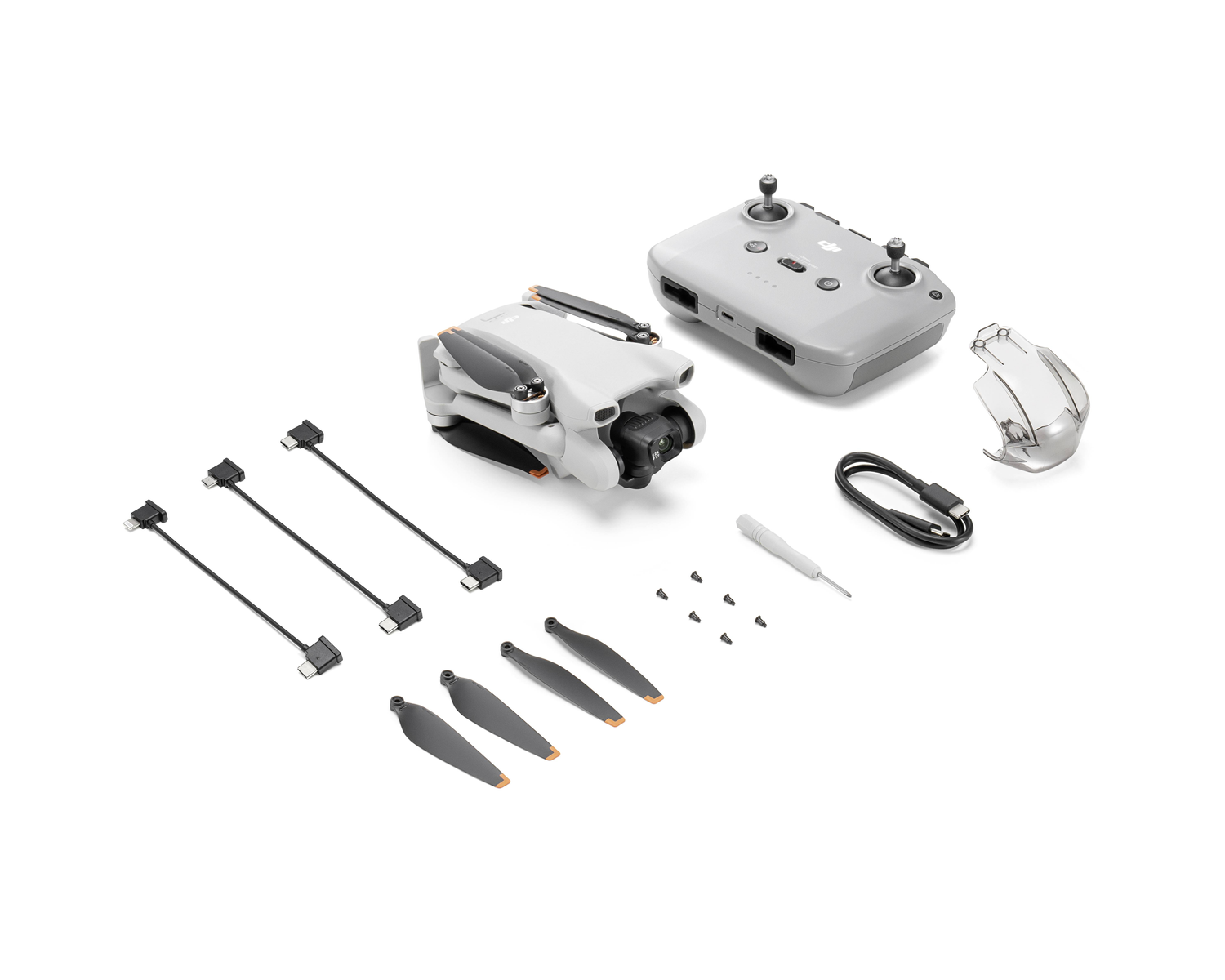 Dron, mando, hélices, cables y accesorios sobre una superficie blanca. El dron es gris y blanco.