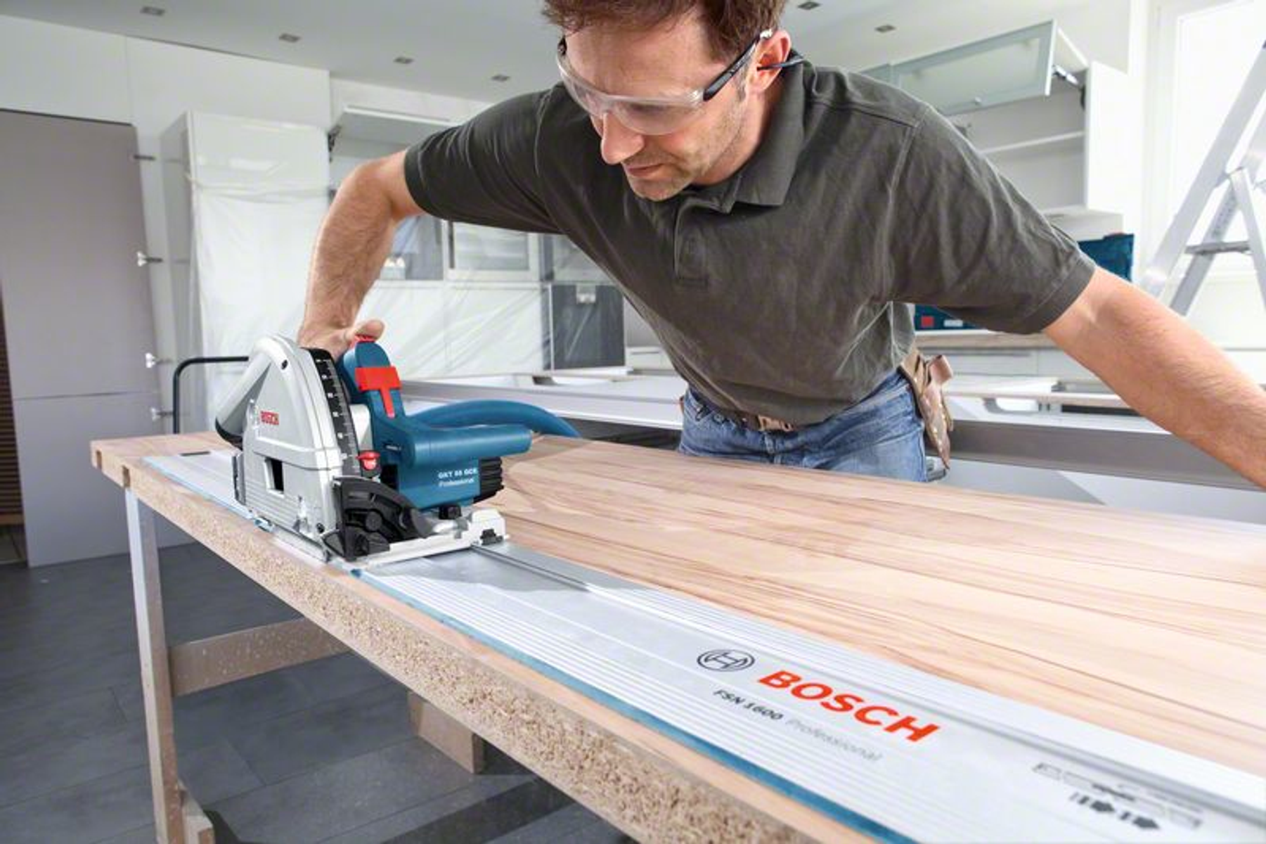 Hombre cortando madera con sierra circular, gafas de seguridad. Madera y armarios detrás.