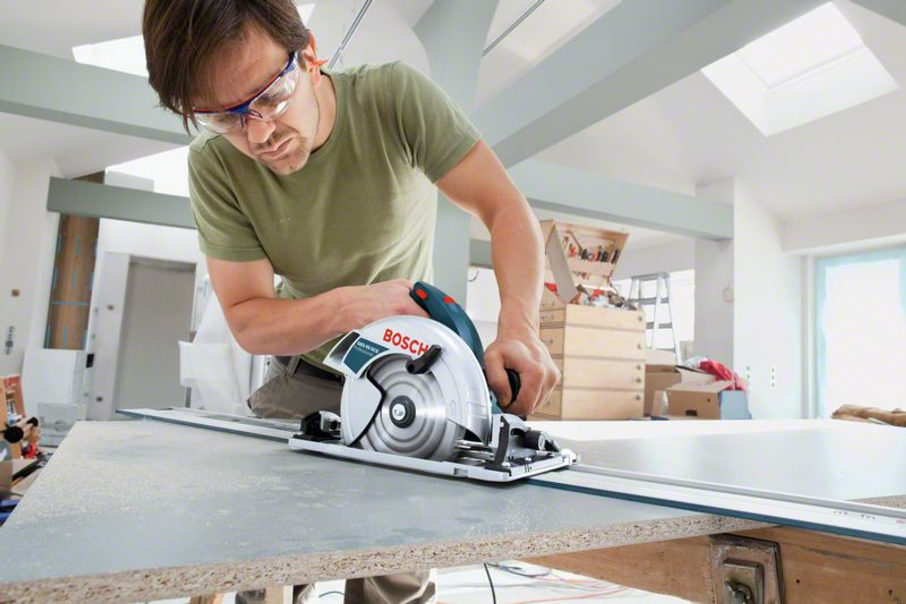 Hombre cortando madera con sierra circular. Usa gafas de seguridad. La sierra está en un banco de trabajo.