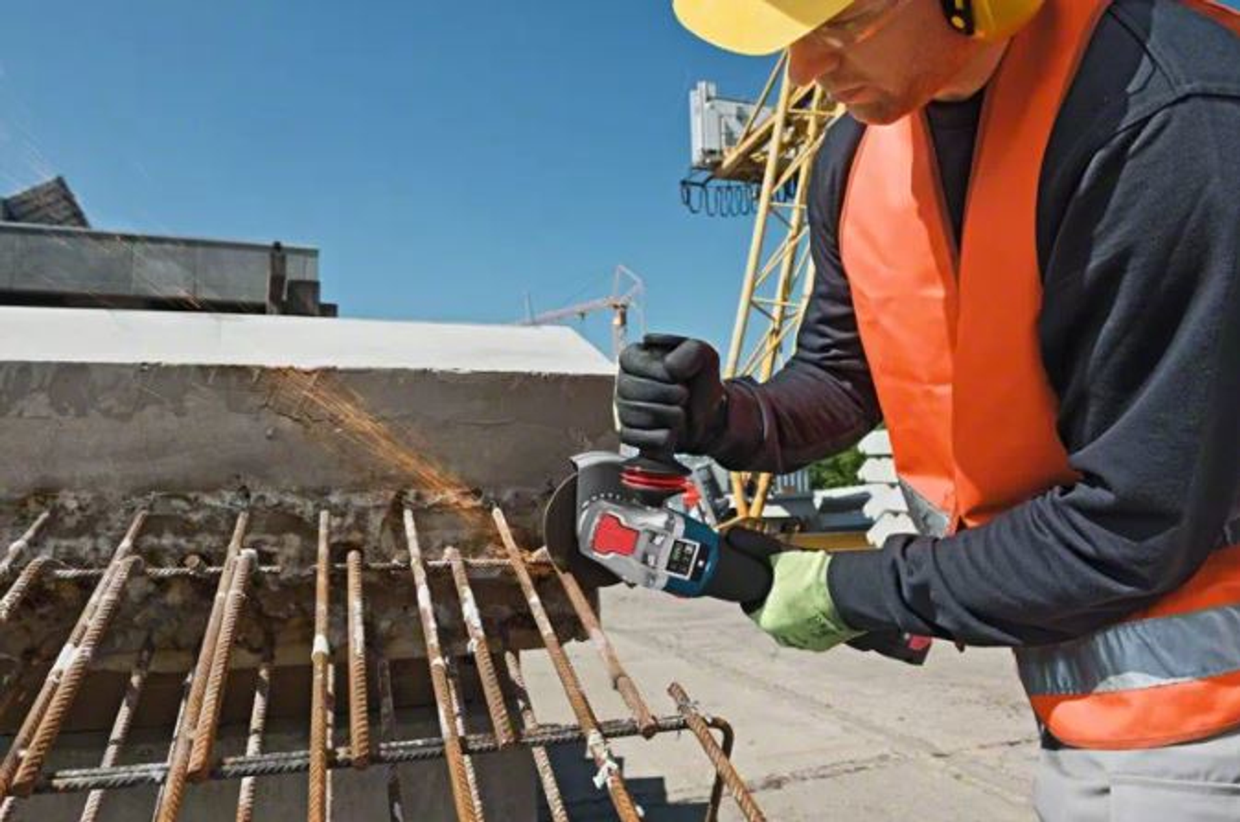 Robotnik używa szlifierki kątowej do cięcia metalowych prętów zbrojeniowych. Iskry lecą podczas pracy na budowie.