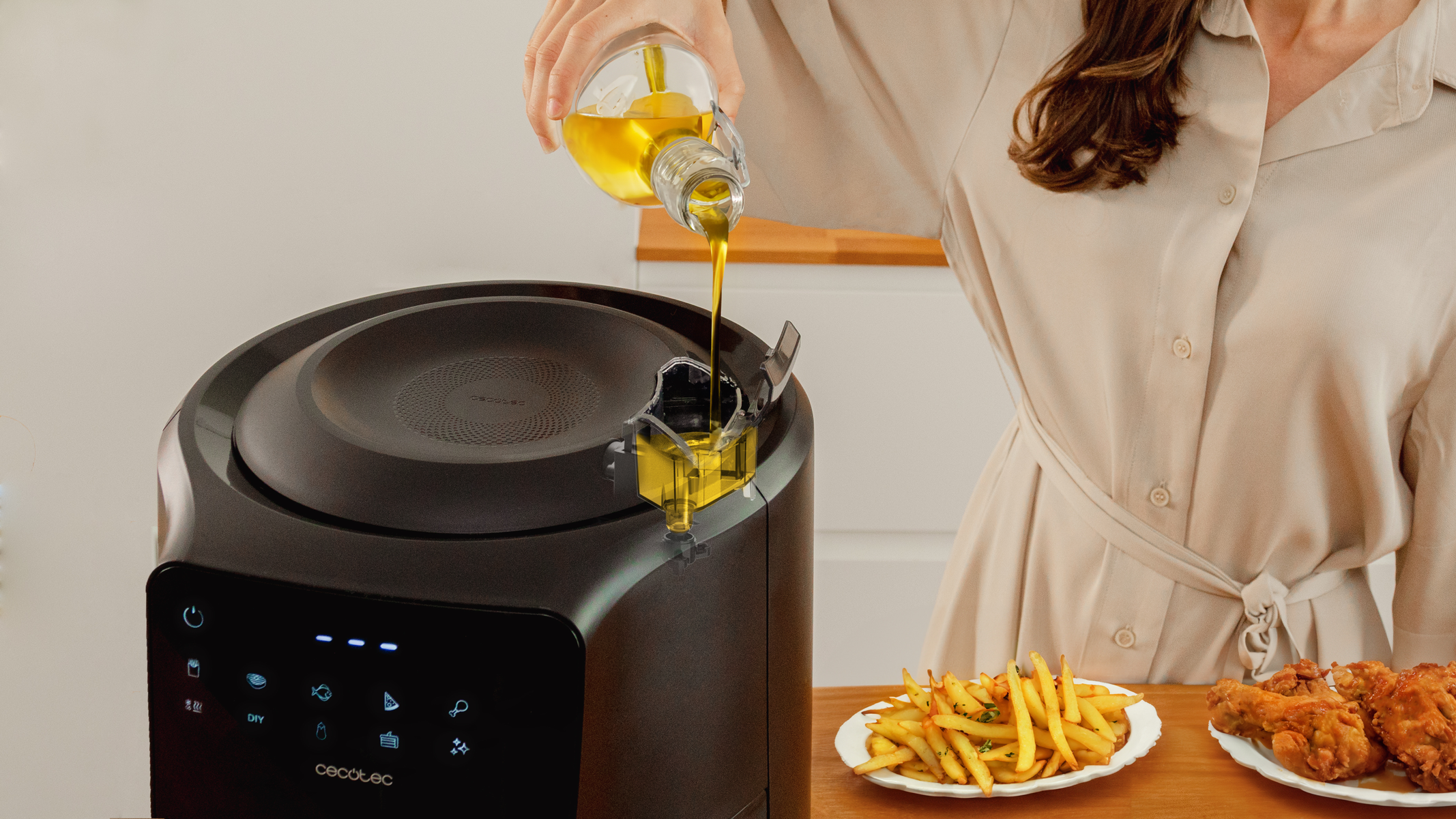Una persona vierte aceite en una freidora de aire. Al lado hay papas fritas y pollo frito.