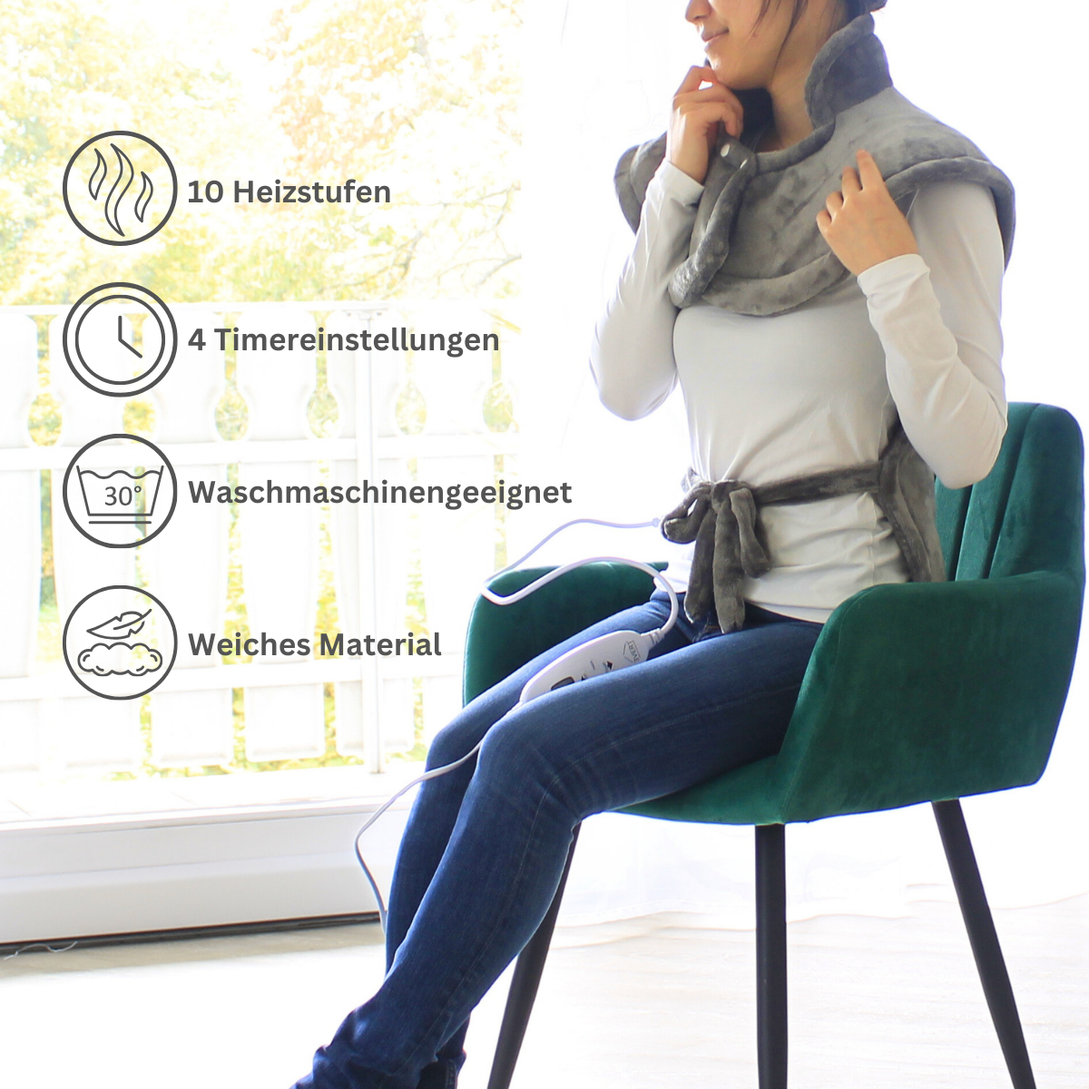 Frau mit grauem Heizkissen um Hals und Schultern, vor einem Fenster. Weißer Hintergrund.
