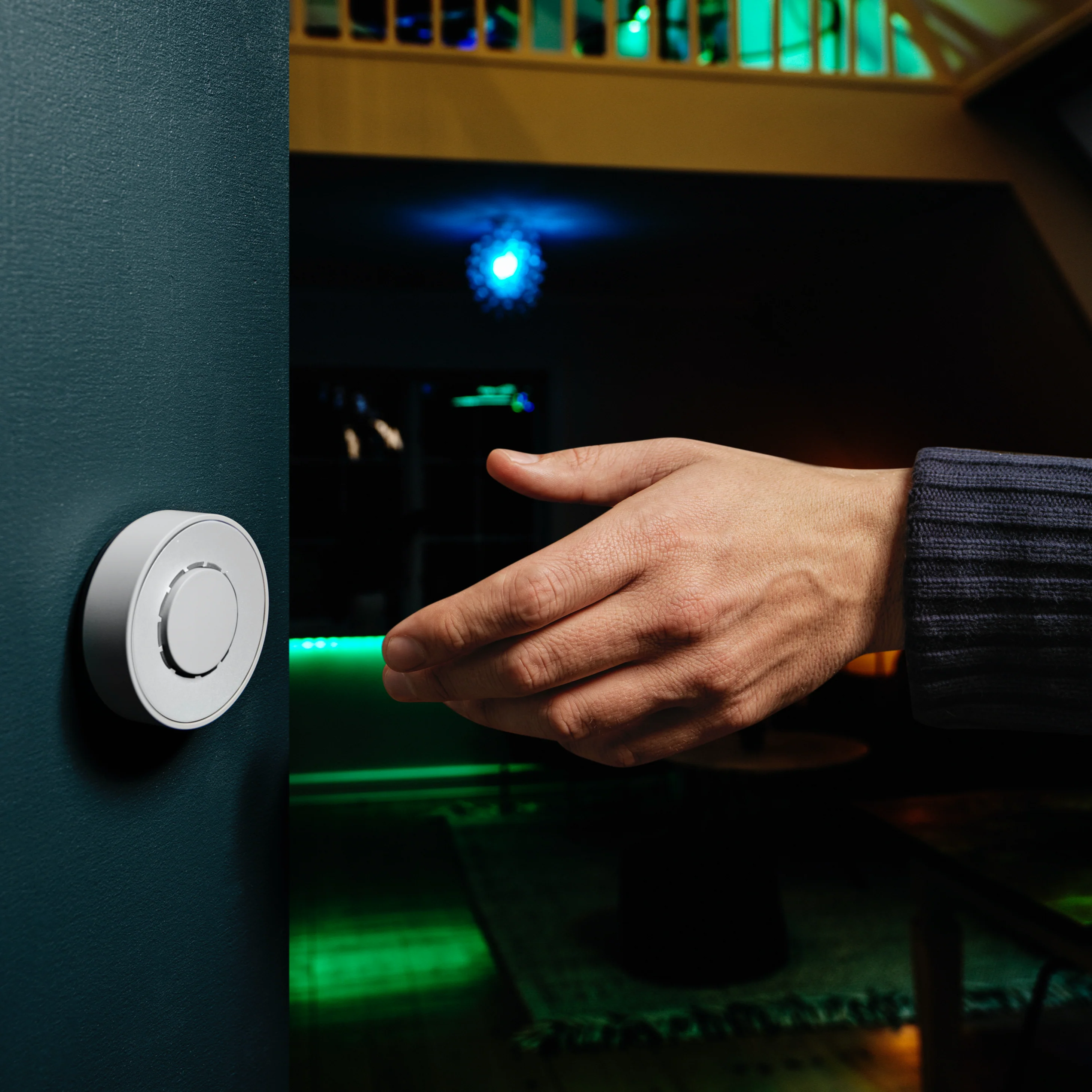Hand reaching towards a white, round device on a teal wall. Dark background.