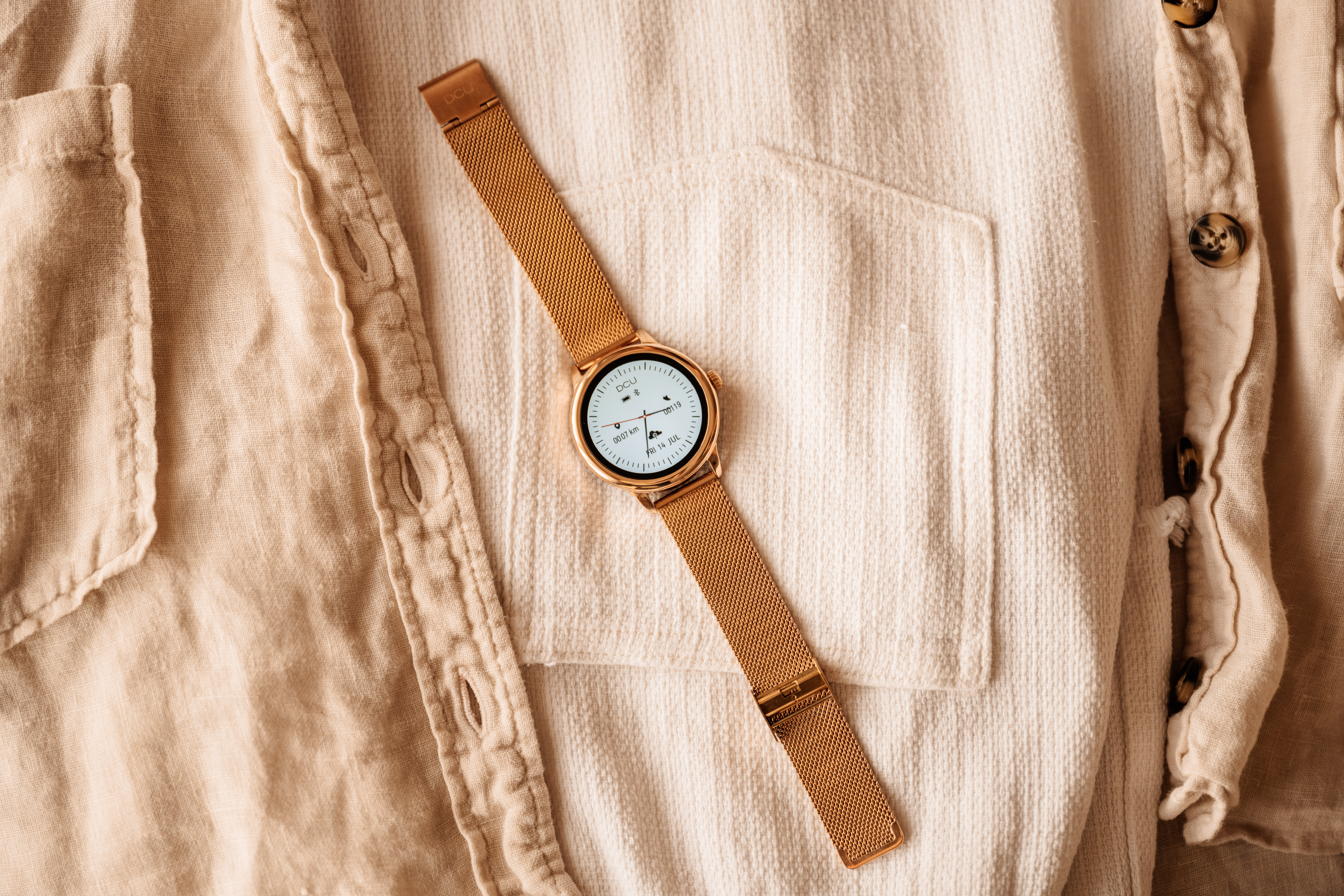 Złoty zegarek na beżowej koszuli. Widok z góry.