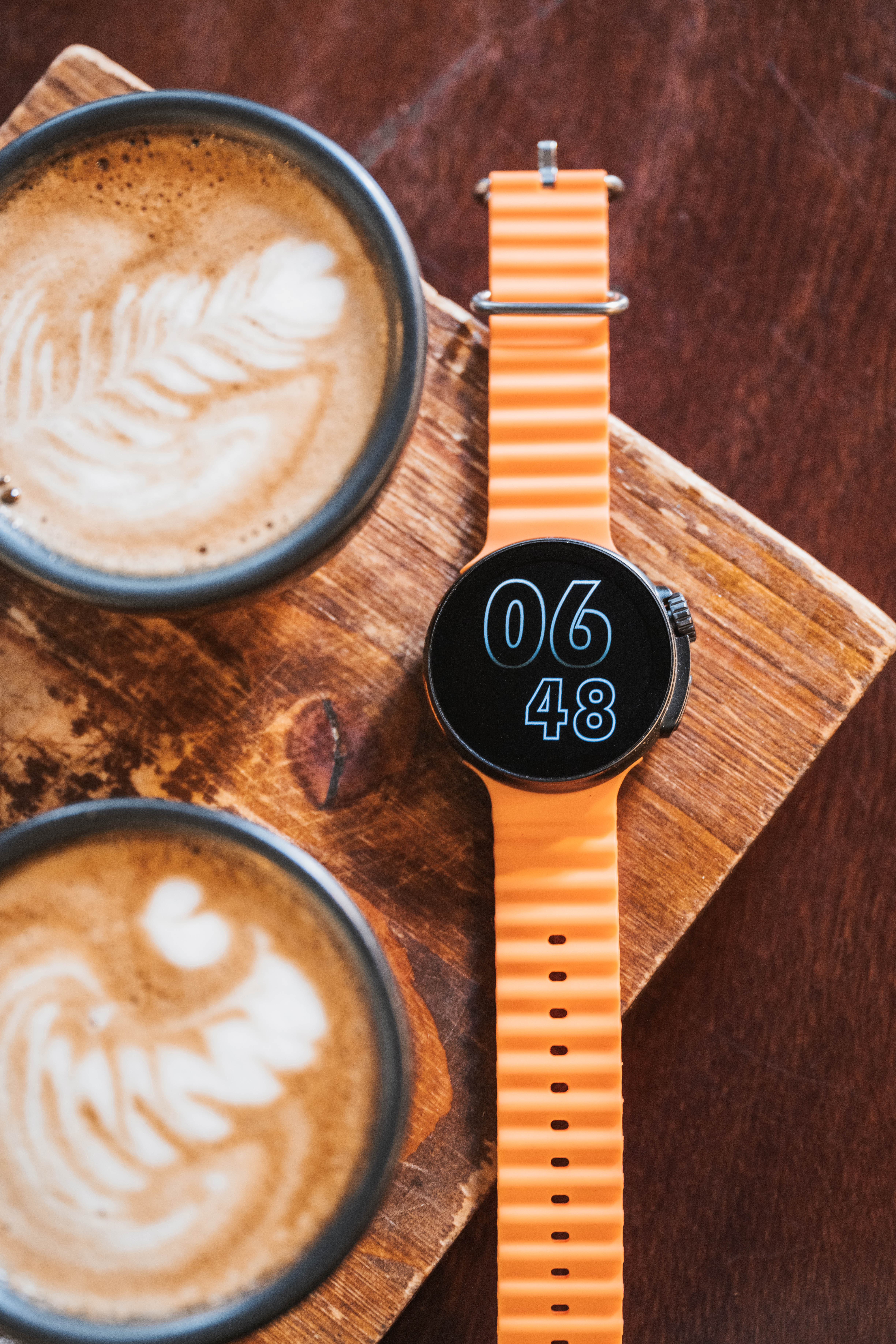 Smartwatch en una tabla de madera con dos tazas de café con latte art.