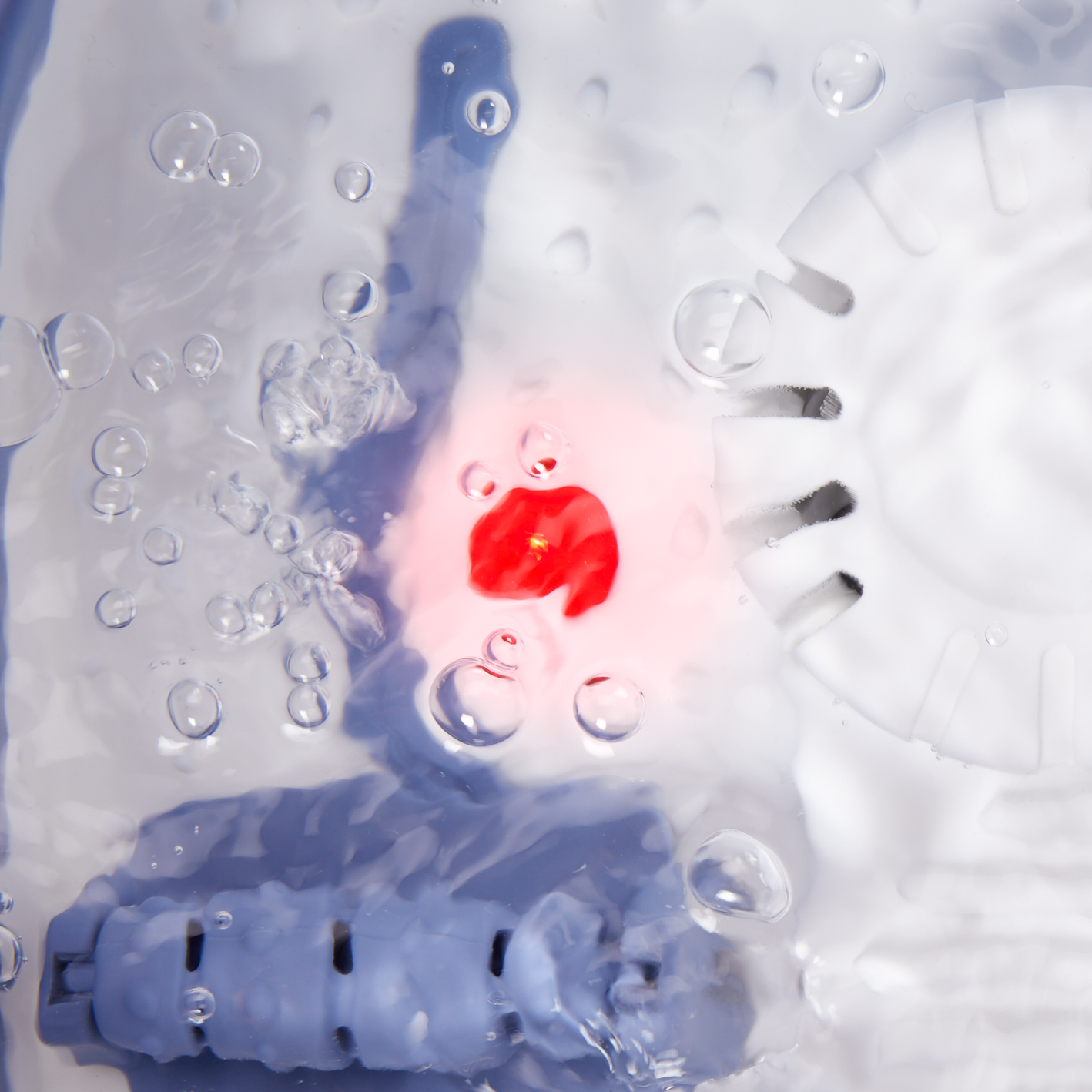 Water with bubbles, red area, and a white circular component, possibly a washing machine interior.