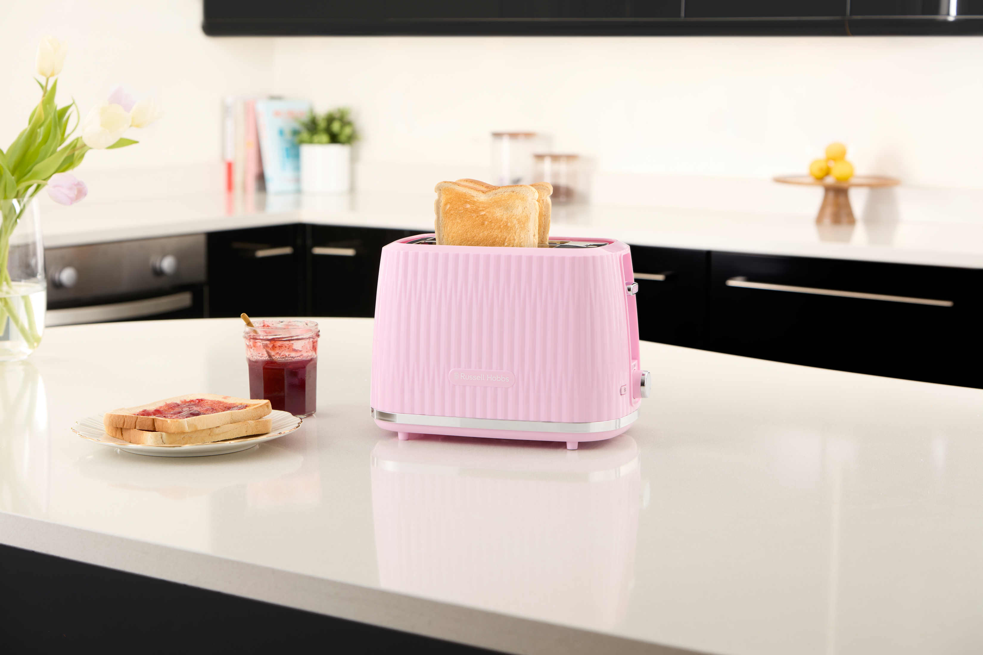 Różowy toster z wyskakującym tostem, z dżemem, tostem i kwiatami w otoczeniu kuchni.