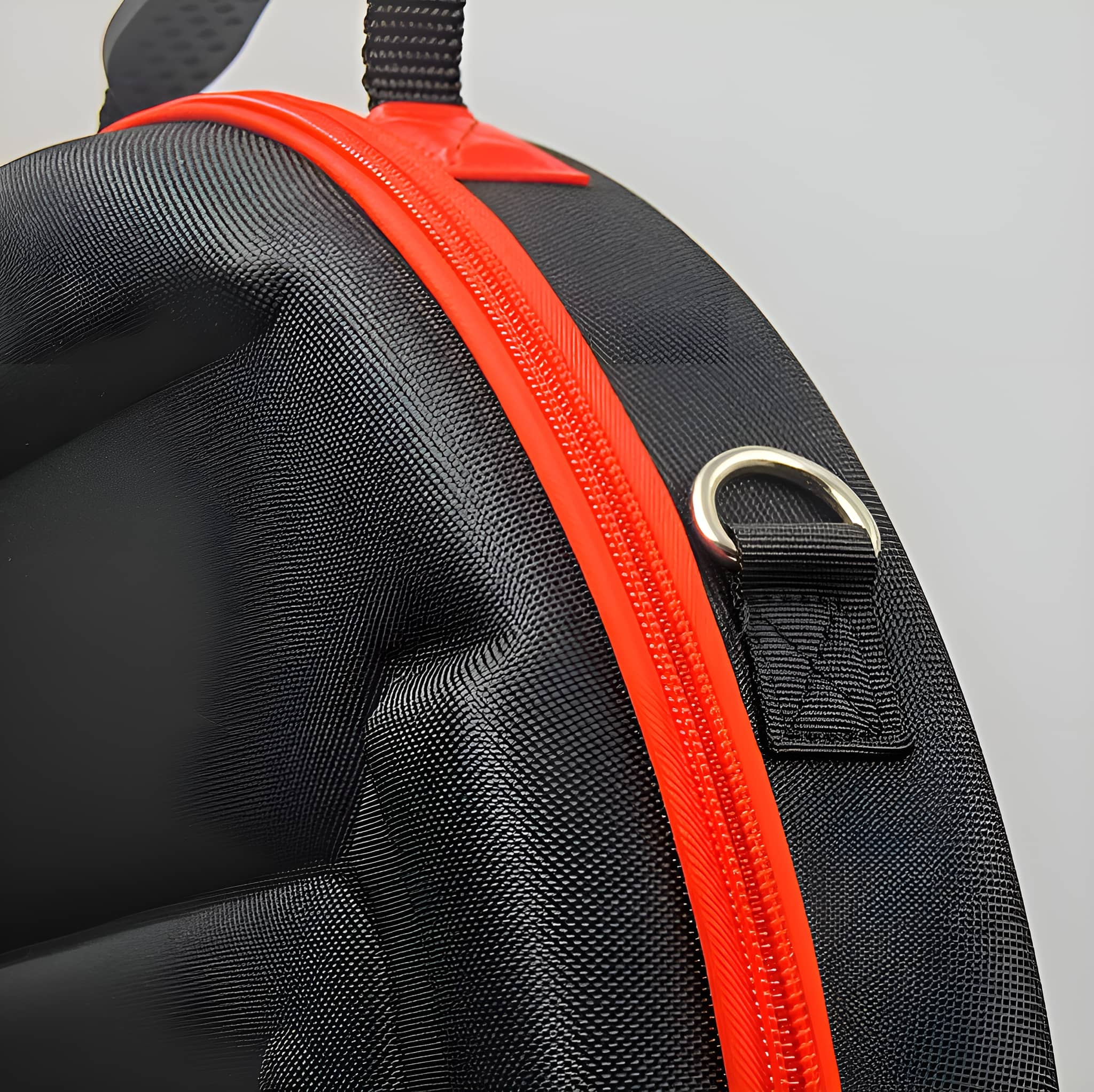 Nahaufnahme einer schwarzen Tasche mit rotem Reißverschluss und Metallring. Die Textur der Tasche ist sichtbar.