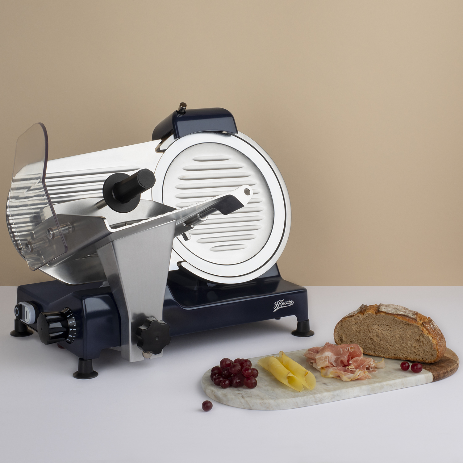 Krajalnica z jedzeniem na marmurowej desce: chleb, ser, mięso i winogrona.