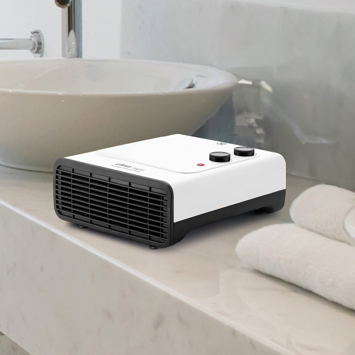 Calentador de baño blanco en una encimera, toallas y lavabo al fondo.