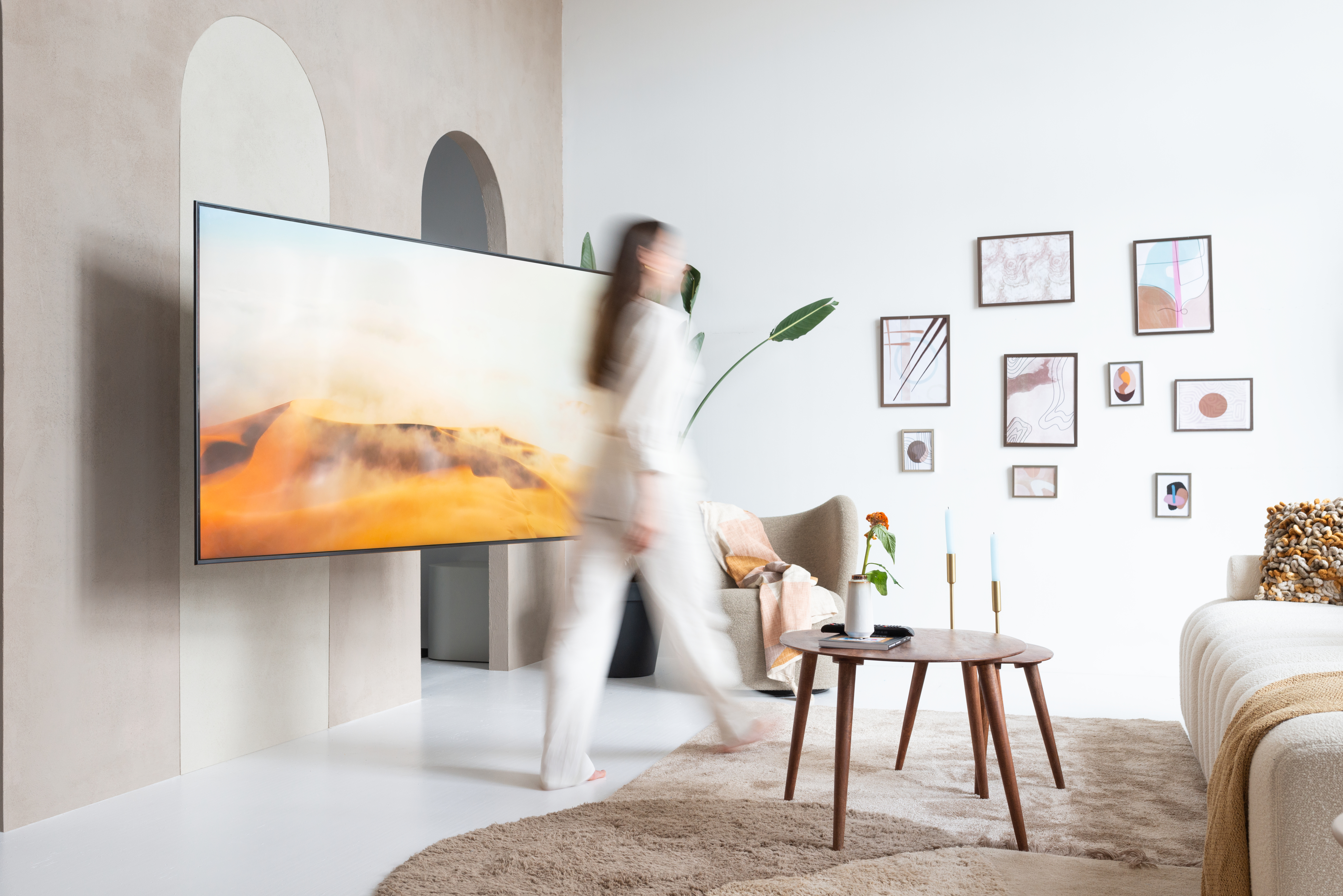 Kobieta przechodzi obok dużego telewizora na ścianie. Wystrój wnętrza z obrazami i meblami.