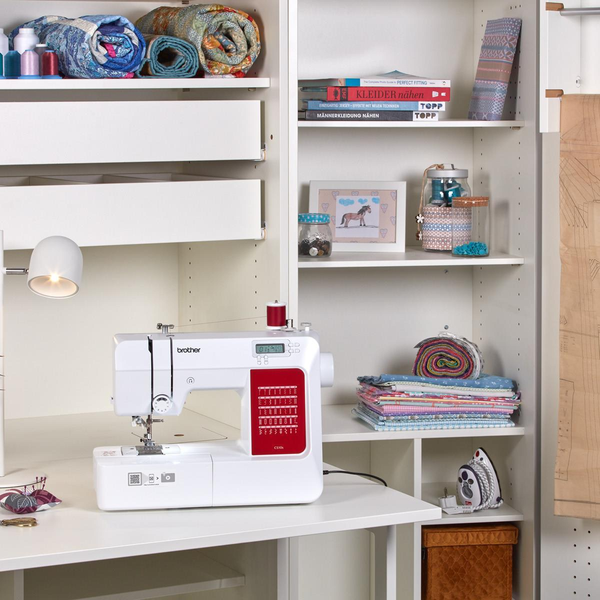 Biała maszyna do szycia na białym biurku w pokoju z półkami pełnymi przedmiotów.