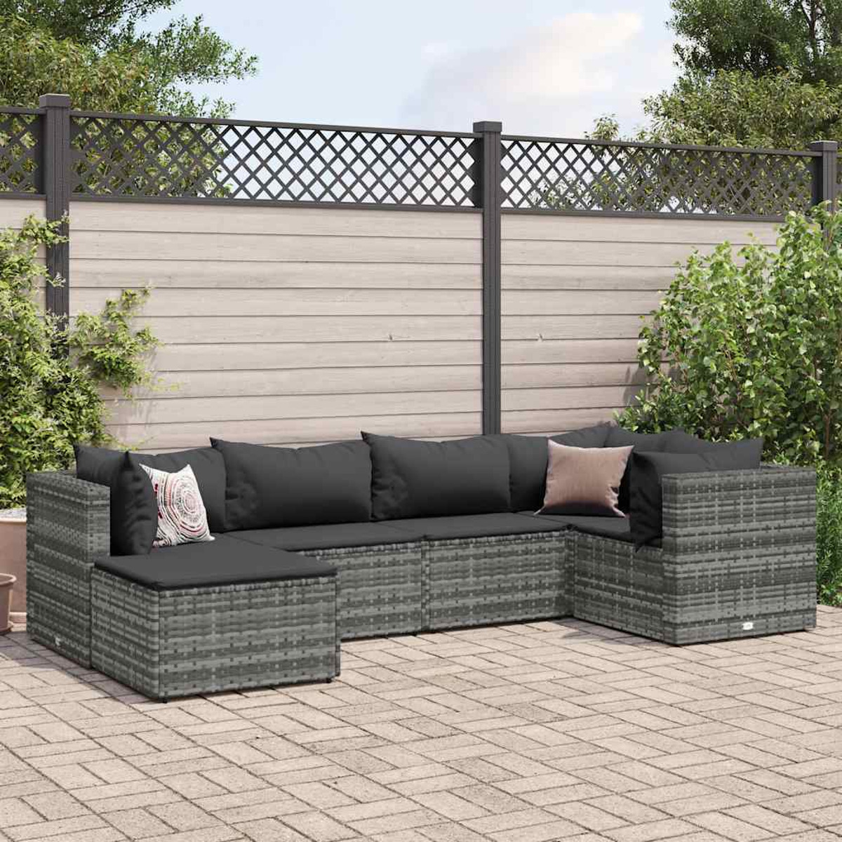 Divano componibile da esterno in rattan grigio con cuscini grigio scuro, su patio in mattoni.