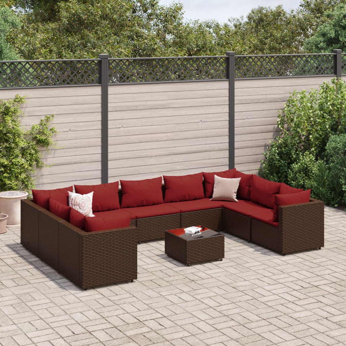 Conjunto de asientos al aire libre. Muebles de mimbre marrón con cojines rojos y almohadas. Patio pavimentado.