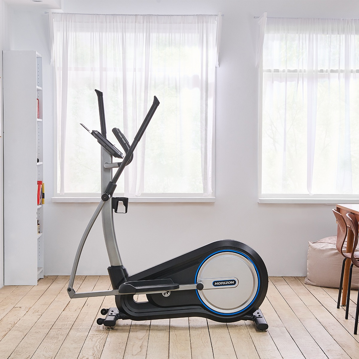 Orbitrek w pokoju z oknami, białą półką na książki i drewnianą podłogą.