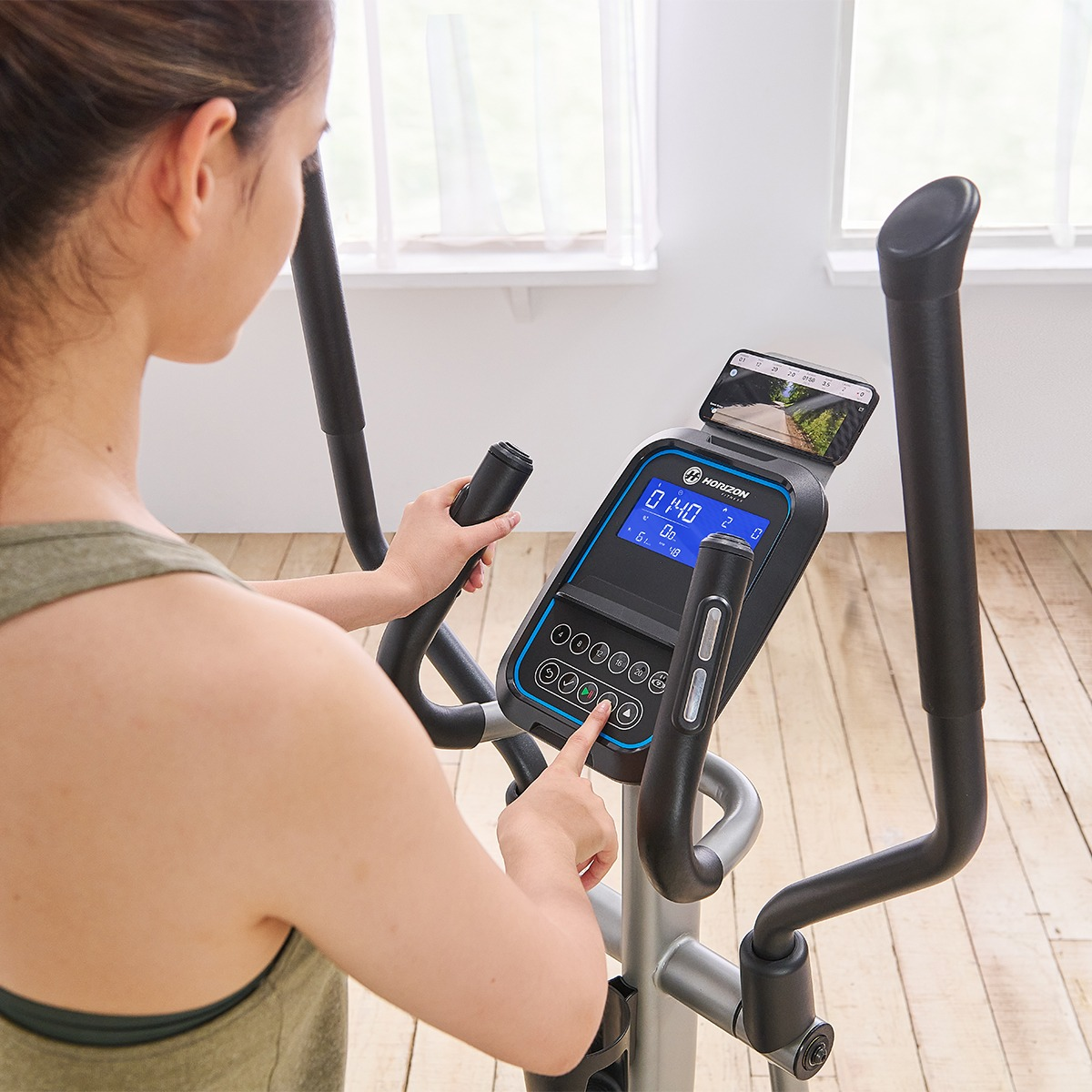 Kobieta korzystająca z orbitreka Horizon, wyświetlająca dane, jasna drewniana podłoga.