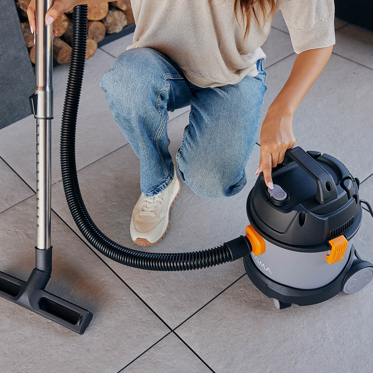 Kobieta używająca odkurzacza. Szary i czarny odkurzacz z pomarańczowymi akcentami.