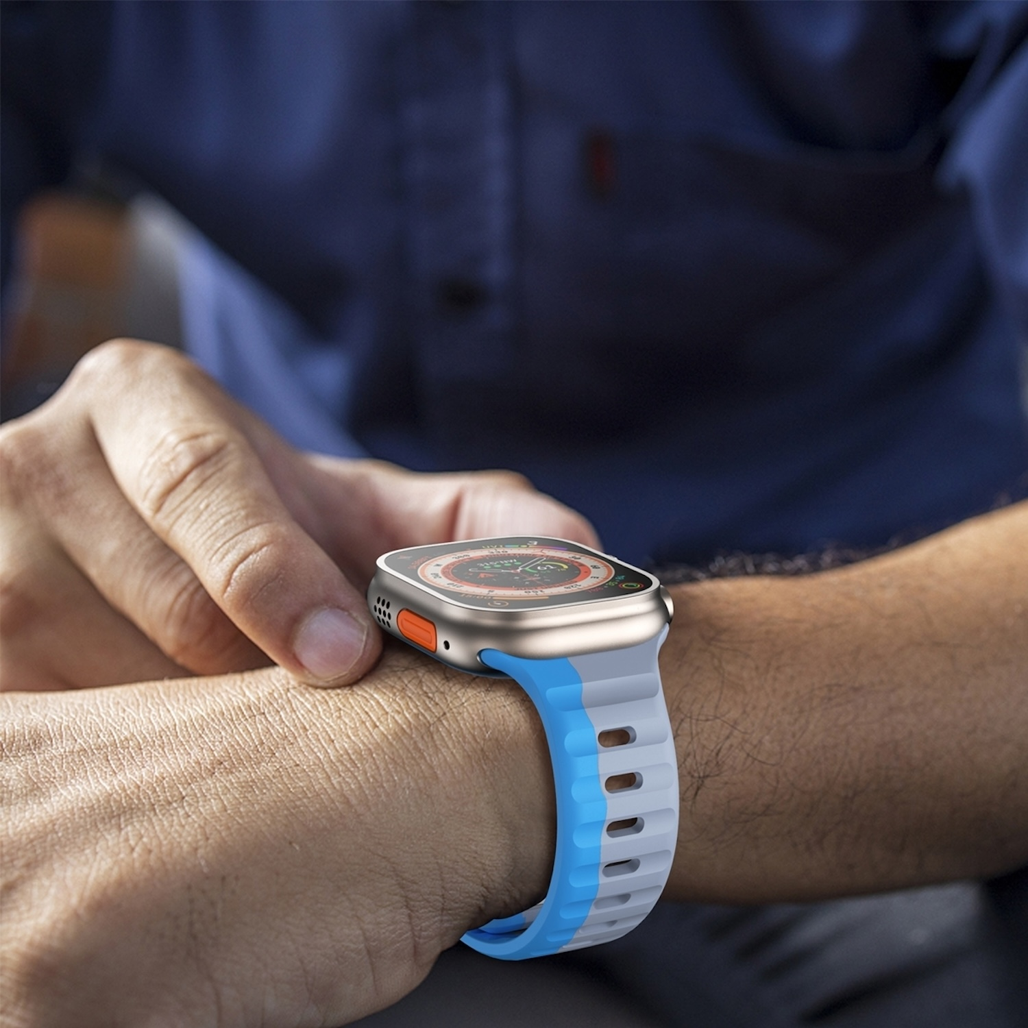 Das Handgelenk einer Person mit einer Smartwatch. Die Uhr hat ein blau-graues Armband und ein silber-oranges Gehäuse.