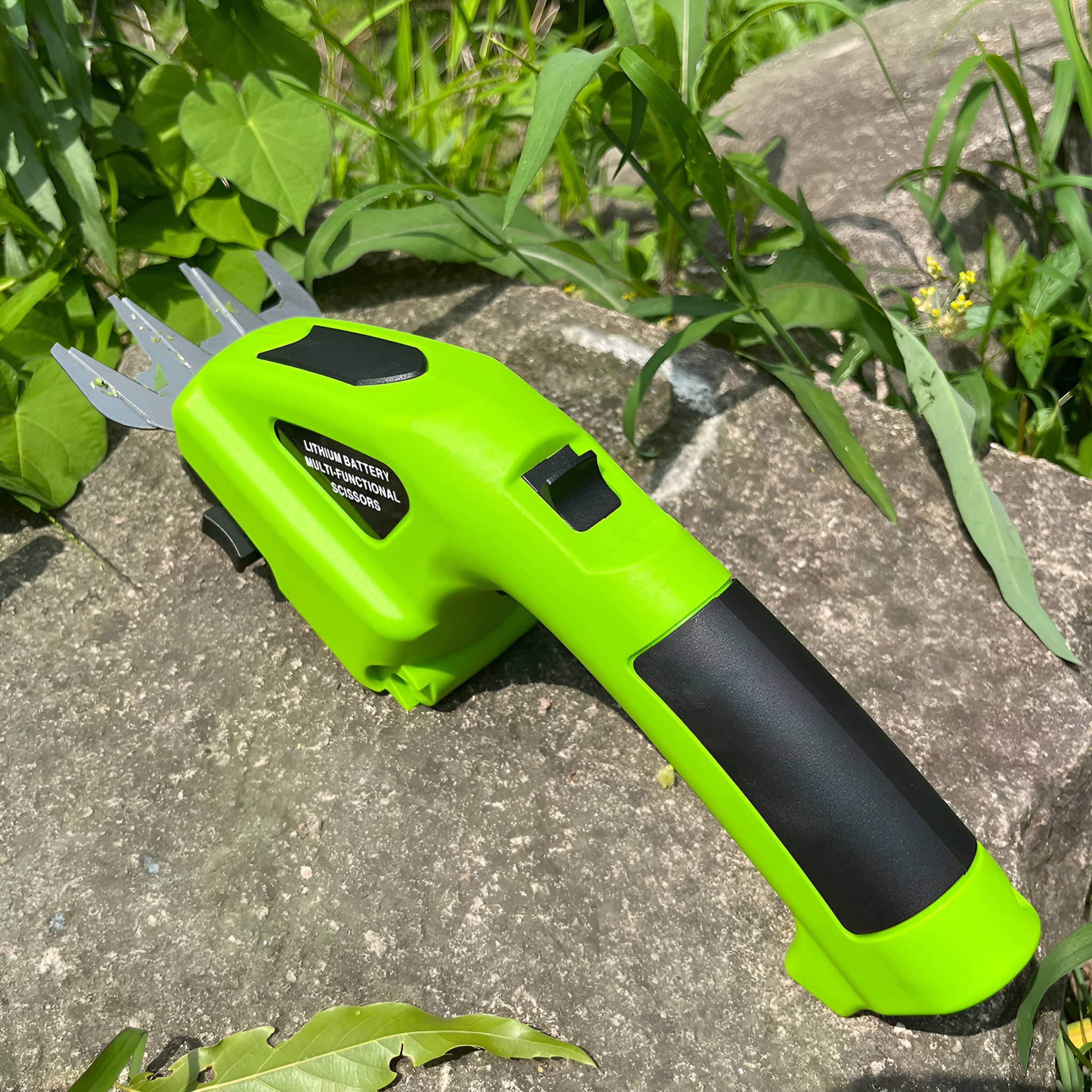 Ein grünes, tragbares Grasscherenwerkzeug auf einer Steinoberfläche, umgeben von grünen Pflanzen.