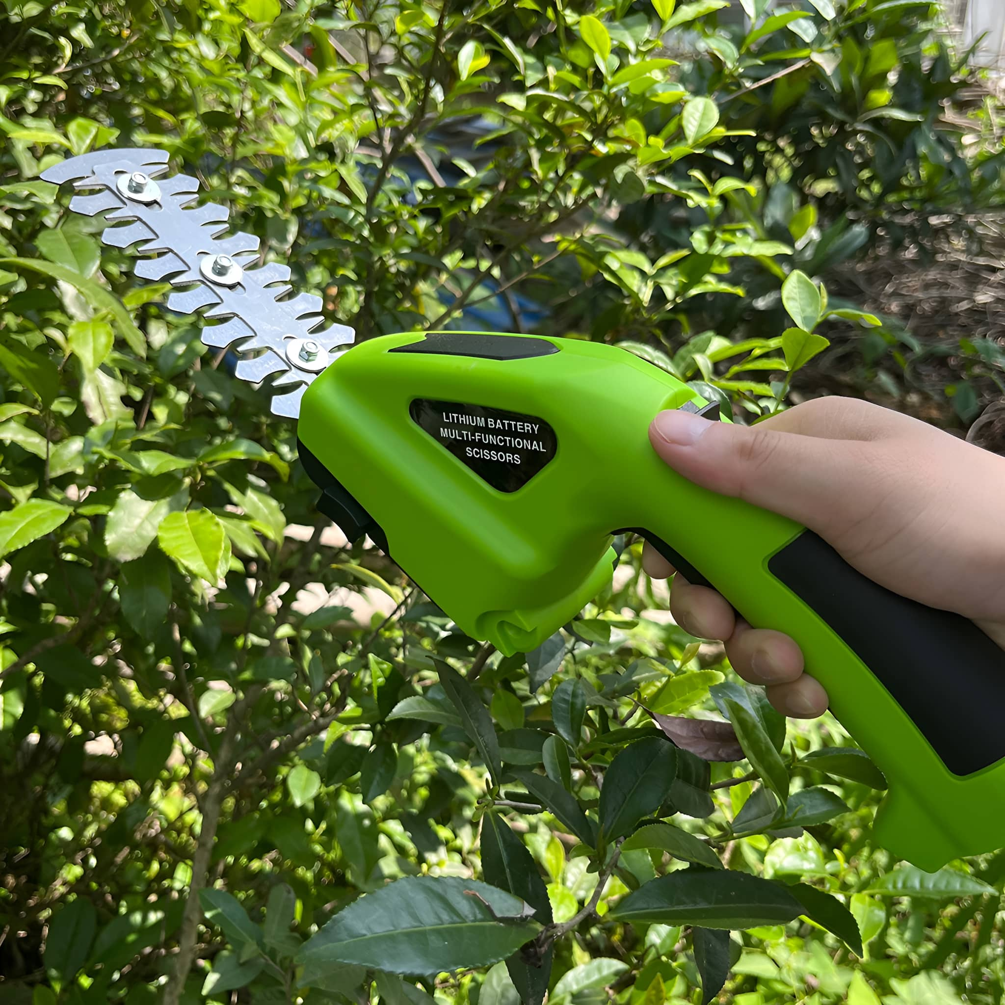 Eine Hand hält einen grünen elektrischen Heckenschneider und schneidet eine grüne Hecke.