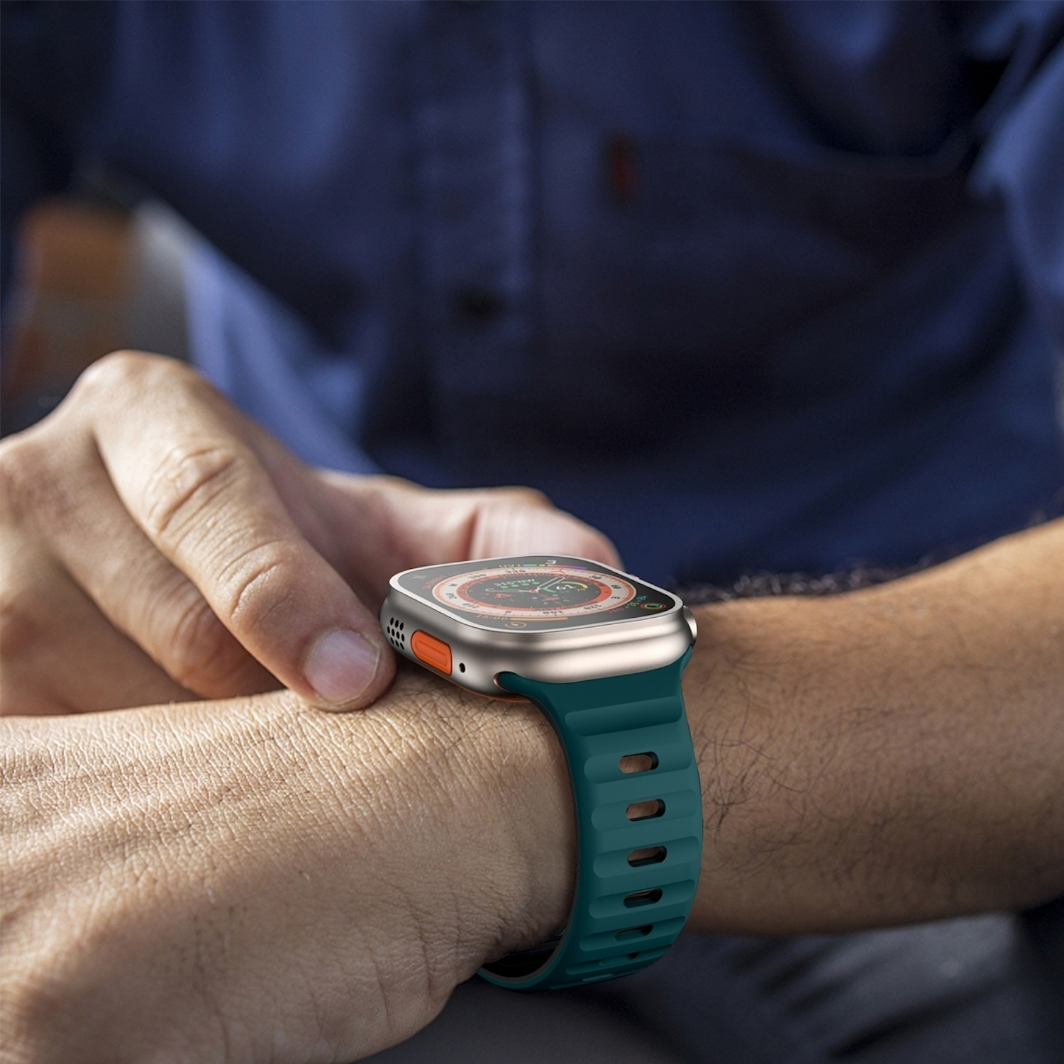 Person trägt eine türkisfarbene Smartwatch. Die Uhr hat eine silberne Lünette und einen orangefarbenen Knopf.