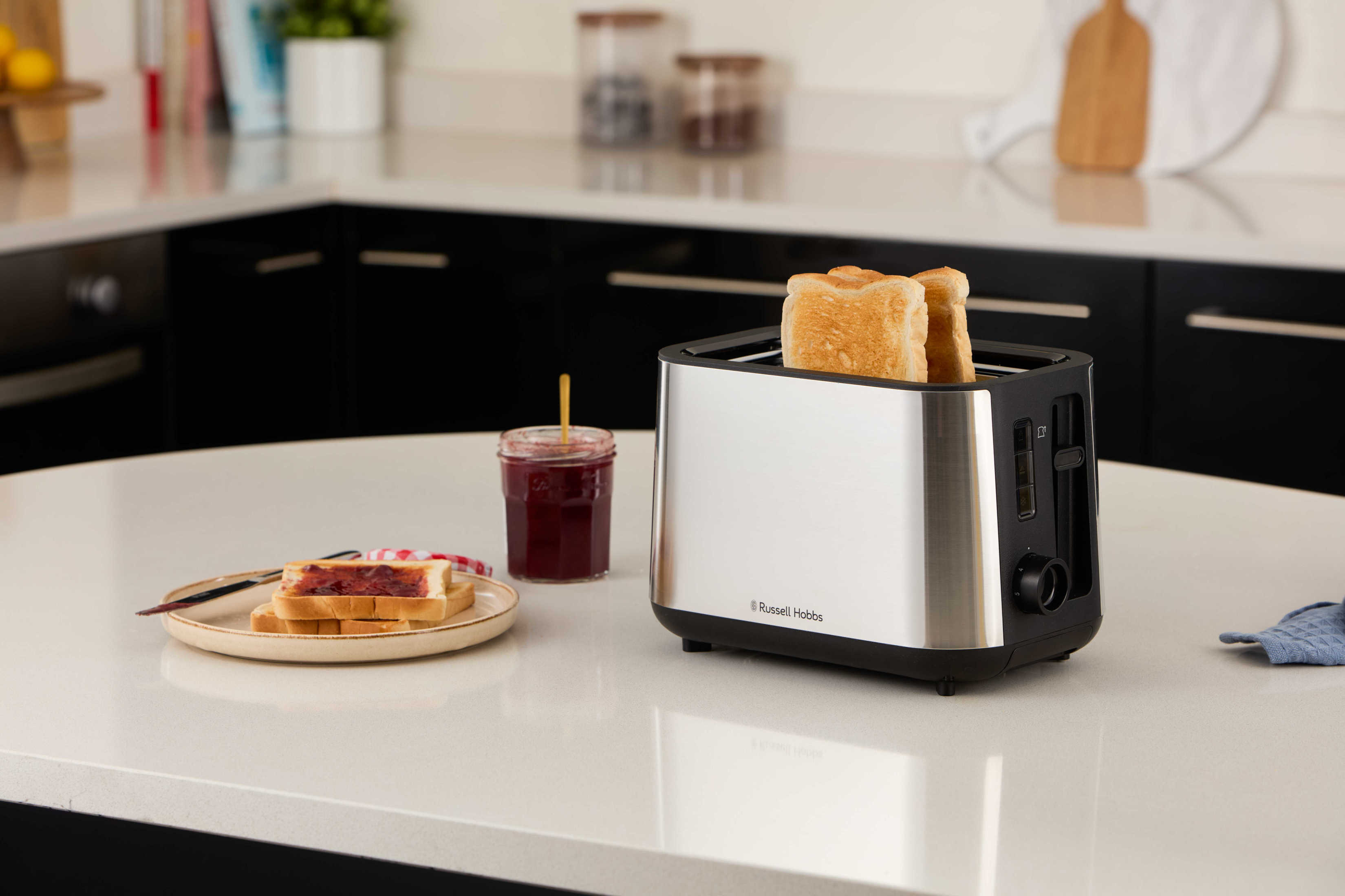 Ein silberner Toaster mit zwei Toastscheiben, Marmelade und einem Toastteller auf einer Theke.