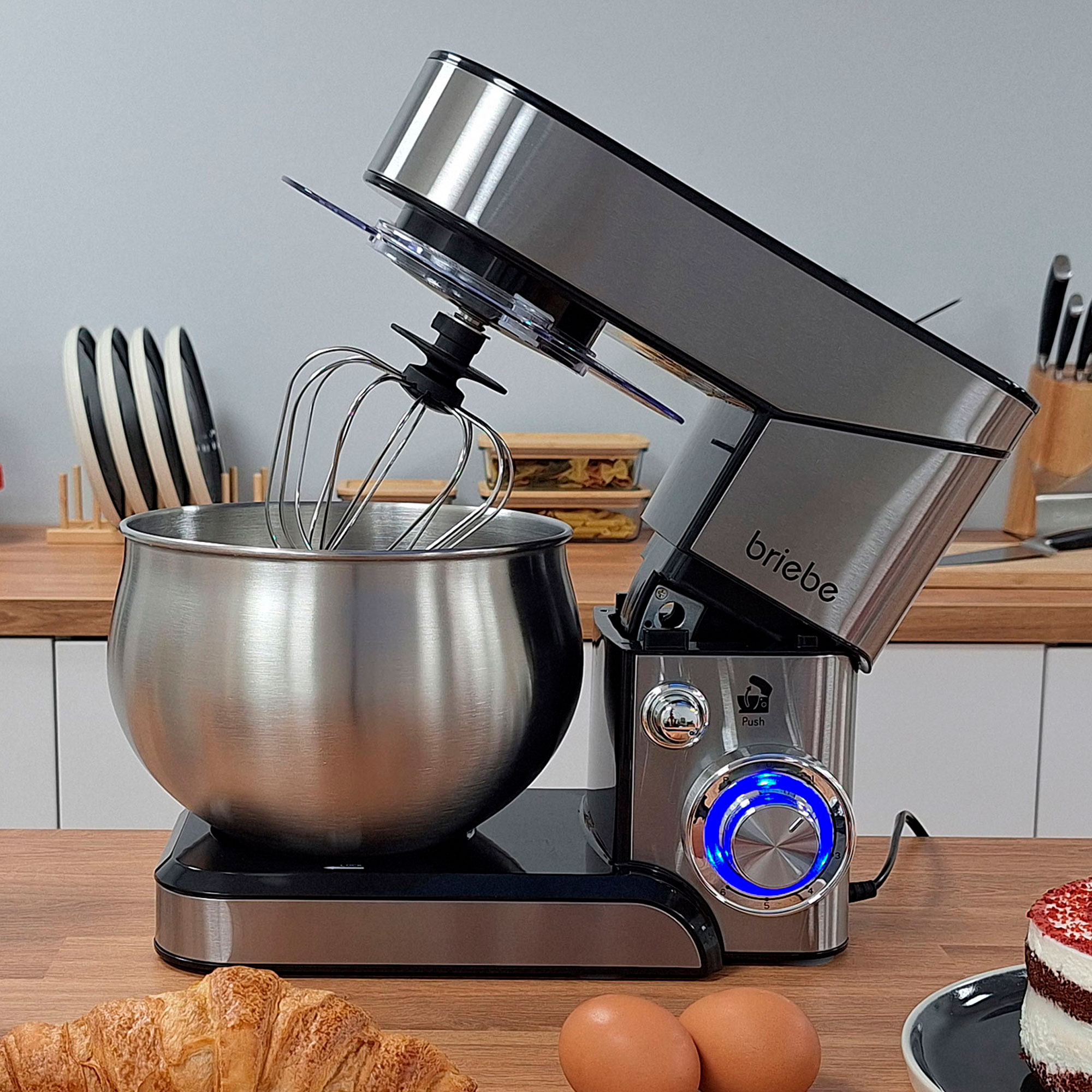 Edelstahl-Küchenmaschine mit Schneebesen und blau beleuchtetem Knopf.